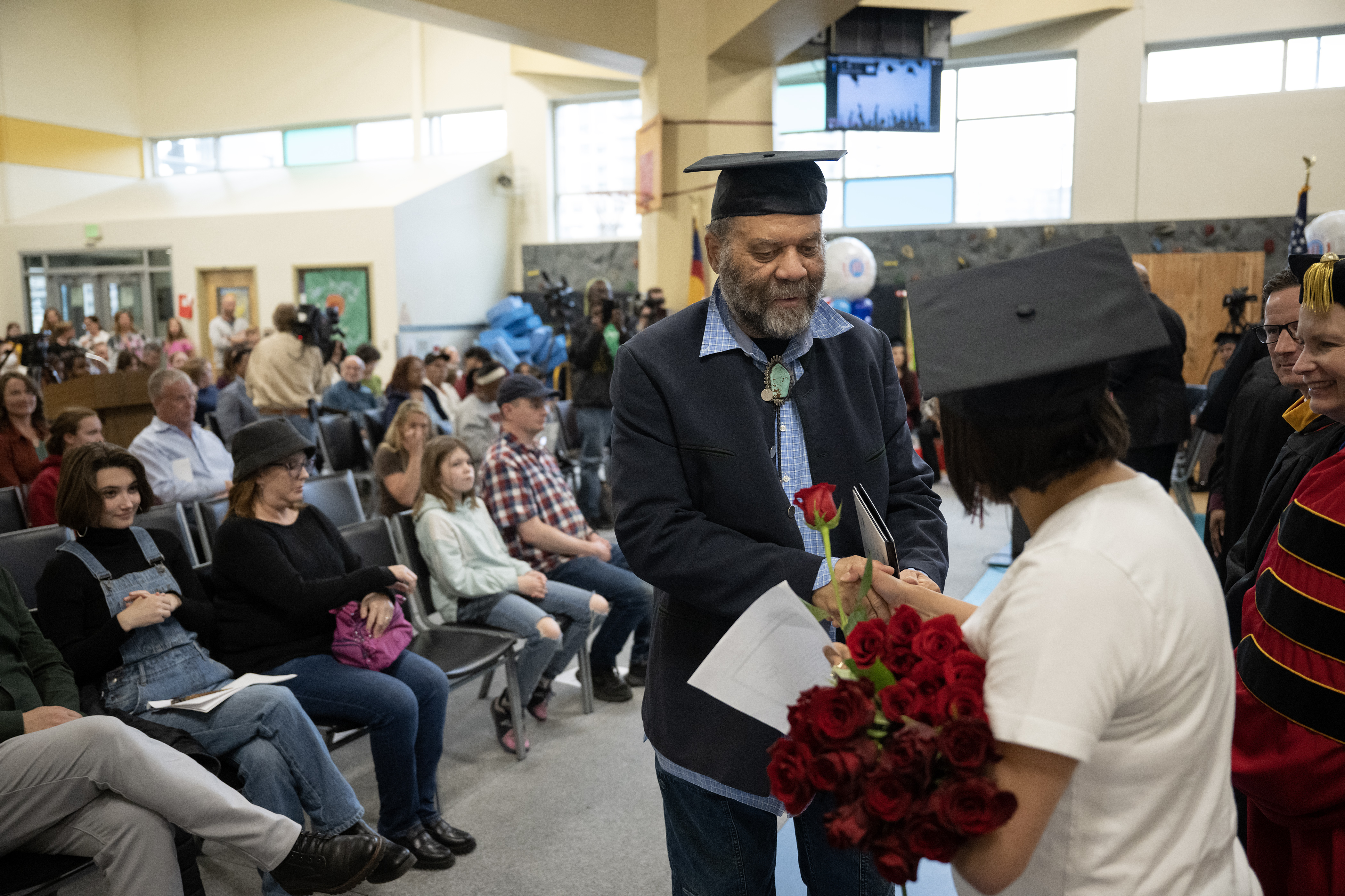 Denver Blues legend Otis Taylor, center, is handed a rose from former Manual High School student Vanessa Quintana after receiving his degree 57 years after being expelled for refusing to trim his afro, during a graduation ceremony where the DPS board would confer degrees to students who’s education was disrupted by the closing of Manual High School in 2006, as well as confer a degree to Taylor on Monday, May 15, 2023, during a Denver Public Schools Board of Education meeting in Denver. (Timothy Hurst/Denver Gazette) (TimHursttim.hurst@gazette.comhttps://secure.gravatar.com/avatar/aca82bd62b4ee425c598527cd6faa1b1?d=mm&r=g)
