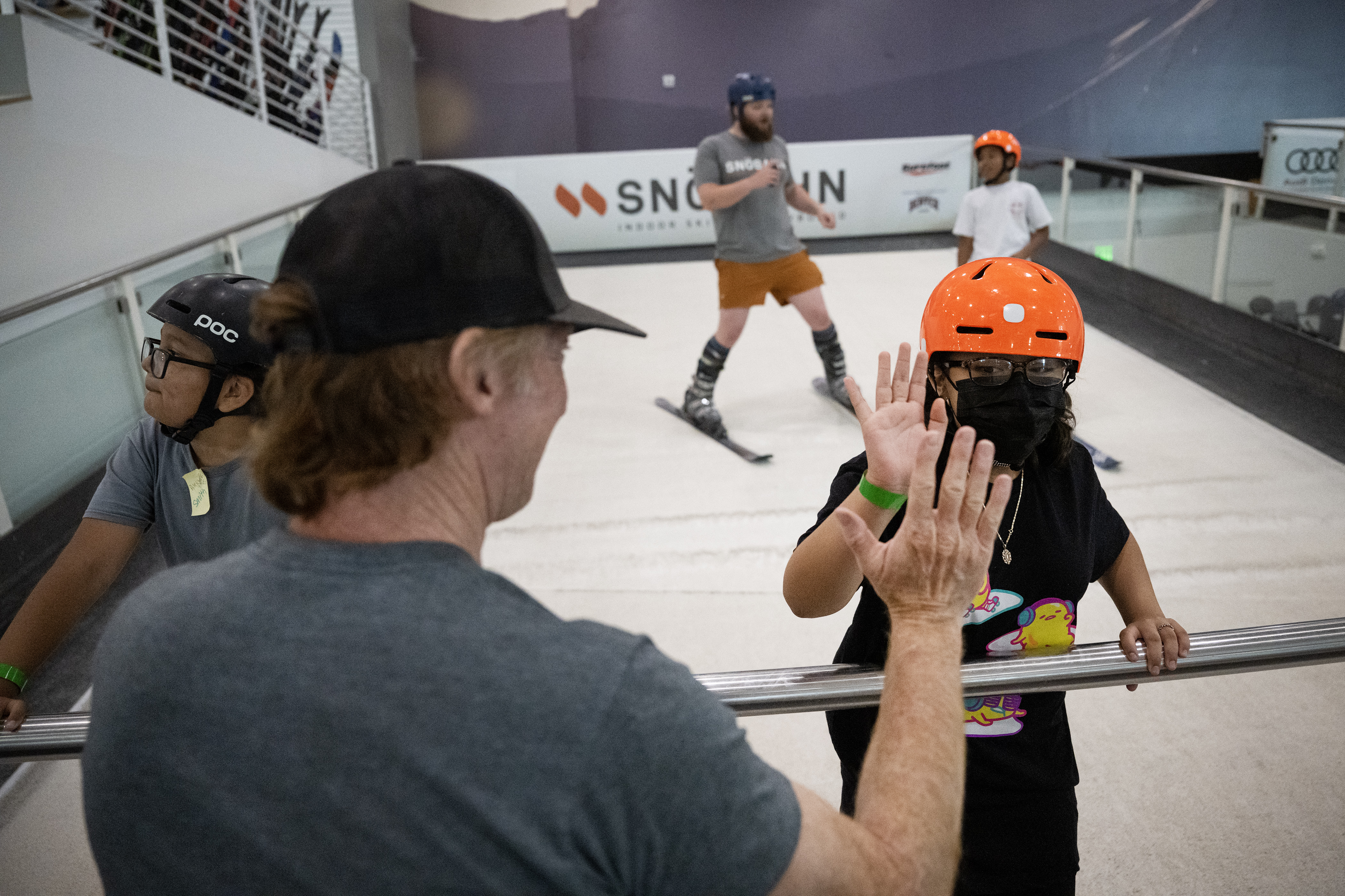Chris Anthony waits at the grab bar to give a high five to fifth grader Kennadie Cervantes as floor lead instructor Payne Smith works with Joshua Atson during the Montbello students’ first ski lesson on one of the indoor revolving slopes as part of Chris Anthony’s Youth Initiative Project on Tuesday, May 23, 2023, at SNÖBAHN Indoor Ski + Snowboard Center in Centennial, Colo. (Timothy Hurst/Denver Gazette) (TimHursttim.hurst@gazette.comhttps://secure.gravatar.com/avatar/aca82bd62b4ee425c598527cd6faa1b1?d=mm&r=g)