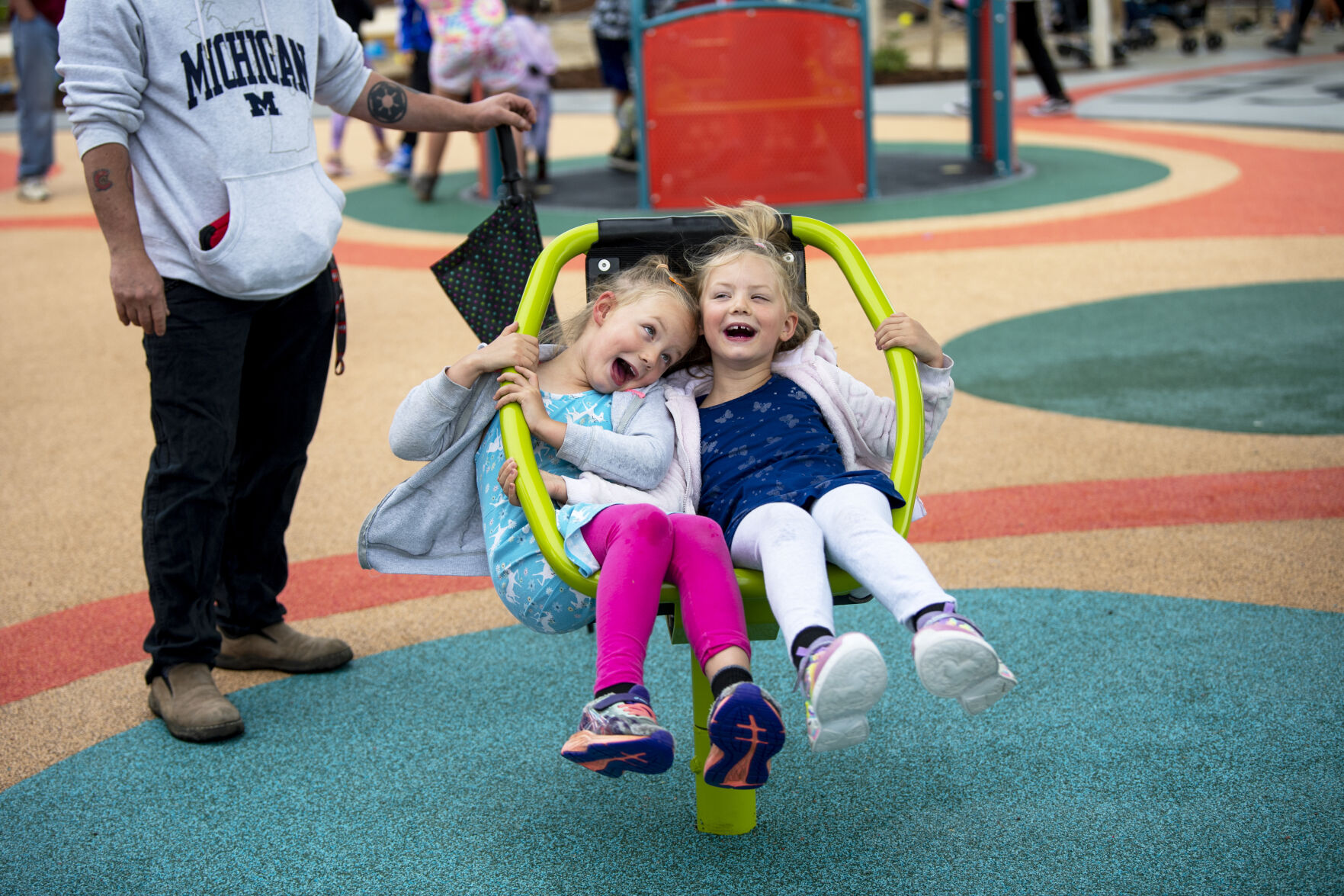 Twin sisters Julie Sanders, left, and Helen Sanders are spun in a chair by their dad at the grand reopening of Panorama Park last summer. (Parker Seibold, The Gazette)
