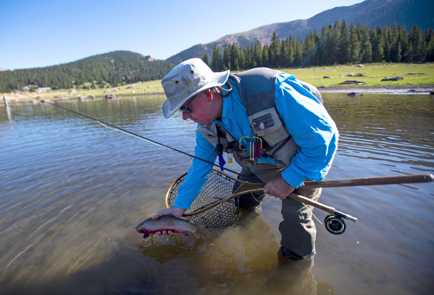 Mike Delaney, a Colorado Springs Utilities employee, reaches into the McReynolds Reservoir to take a cutthroat trout off his line on Thursday, July 11 at the South Slope Recreation Area. The employee is one of a number of regulars that make up a large percentage of those that purchase permits to the recreation area. (The Gazette, Parker Seibold)