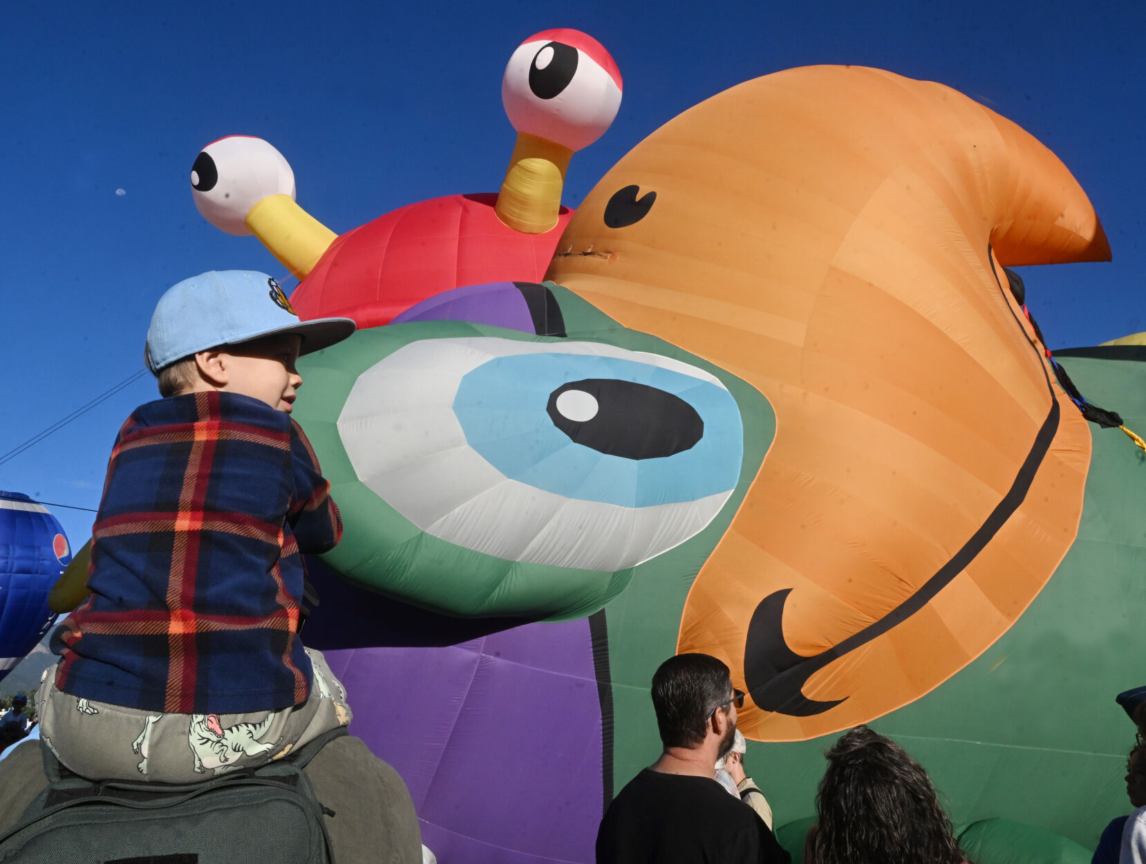 Quinn Reilly sits on his father’s shoulders to get a better look at the Peg Leg Pete the Pirate Parrot balloon inflating as the crab balloon peeks over the top. The parrot balloon was one of the new kids on the block for this year’s Colorado Springs Labor Day Lift Off. The balloons didn’t lift off on Sunday morning, because of winds at higher altitudes, but most still participated with a stationary inflation to please the thousands on Sunday, Sept. 3, 2023. (Jerilee Bennett, The Gazette)
