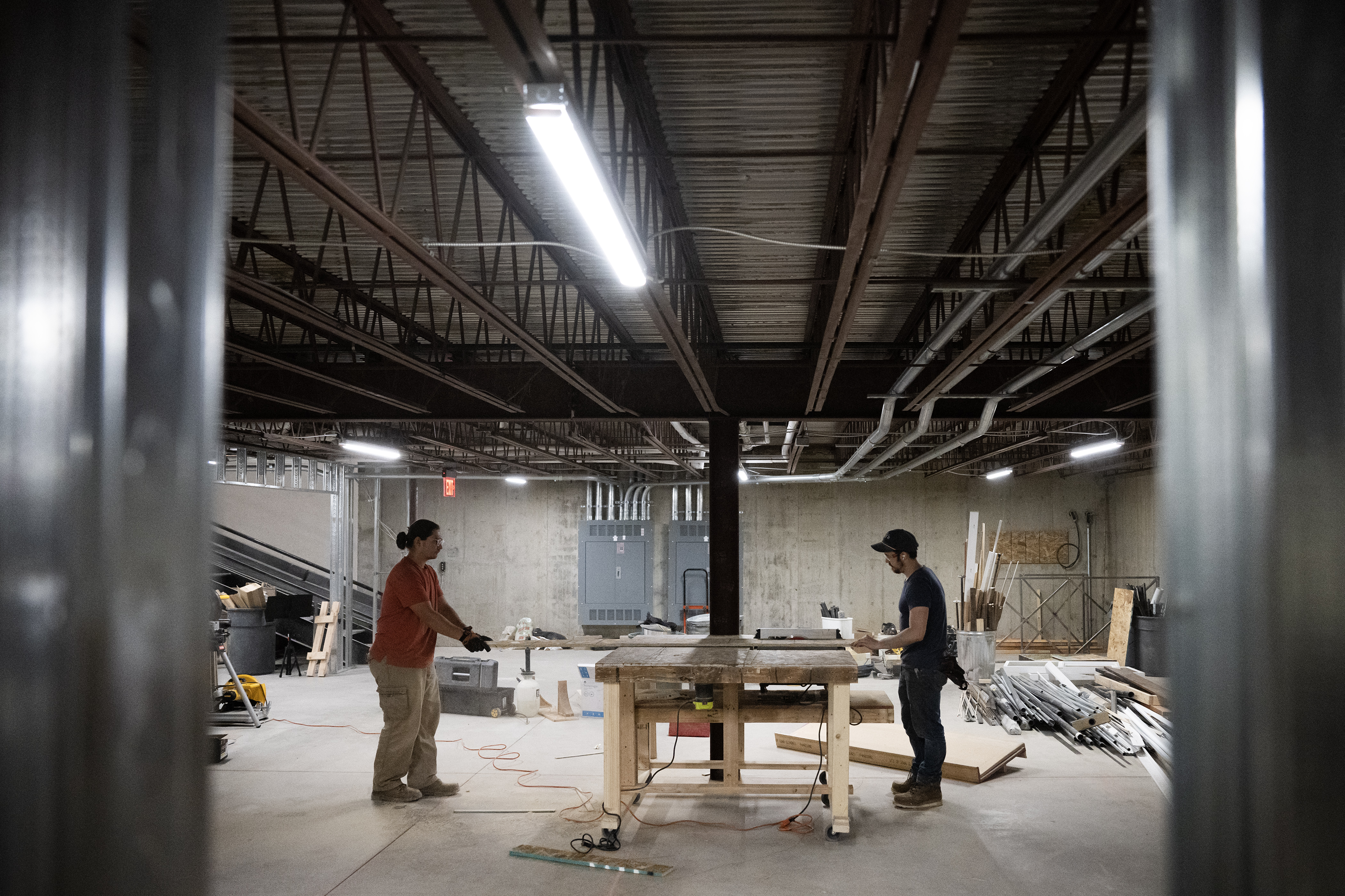 Tanis Gonzales, left, and John Hauser cut down sheets of particleboard in the spacious basement shop for the set of
