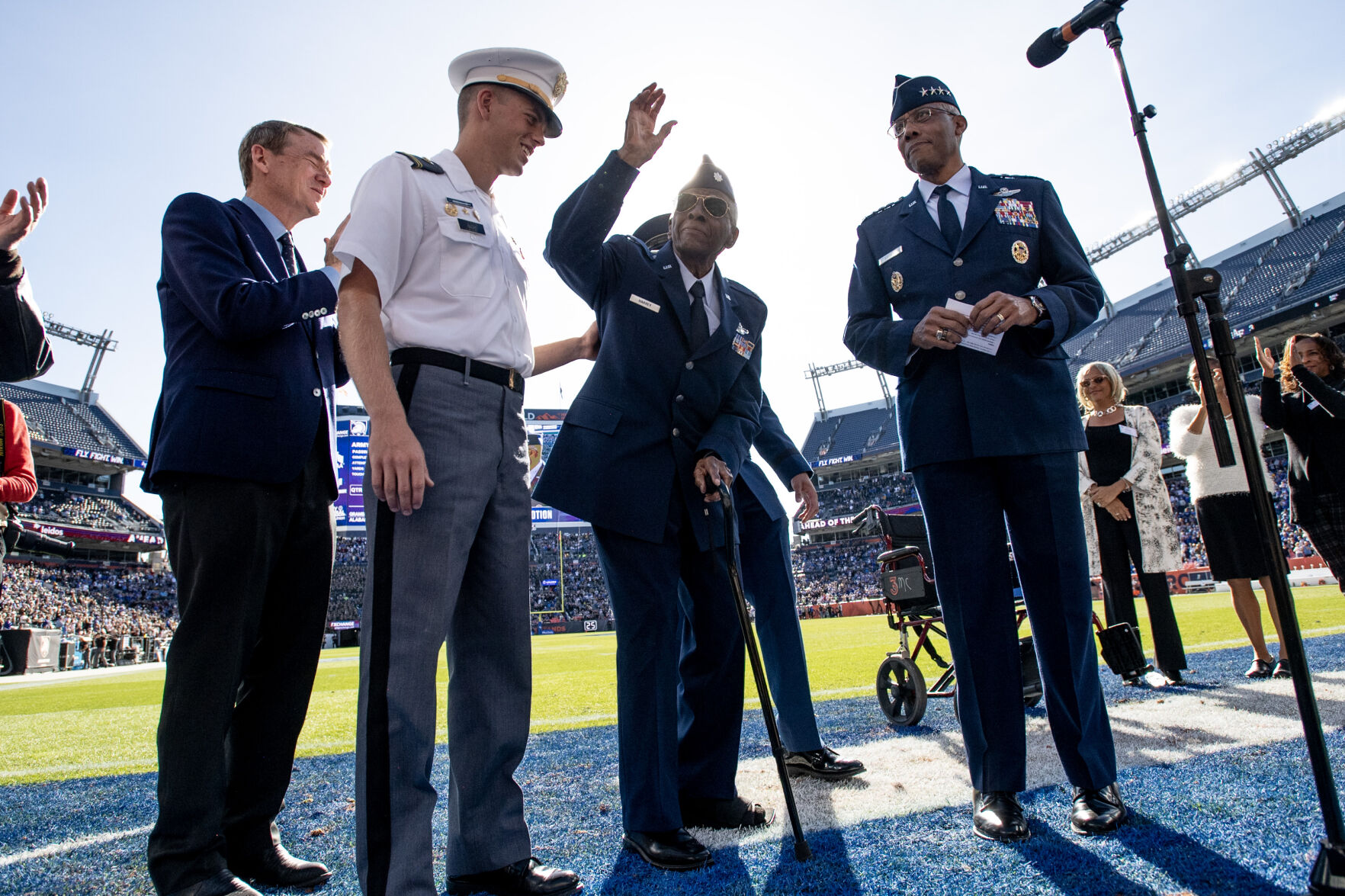 Tuskegee Airman Lt. Col. James Harvey III, center, waves to the crowd during halftime of the Air Force-Army game on Saturday at Empower Field at Mile High in Denver. Harvey, a WWII and Korean War veteran, was given an honorary promotion to the rank of colonel presented by Sen. Michael Bennett, far left, and Gen. Charles Q. Brown, right. (Parker Seibold, the gazette)