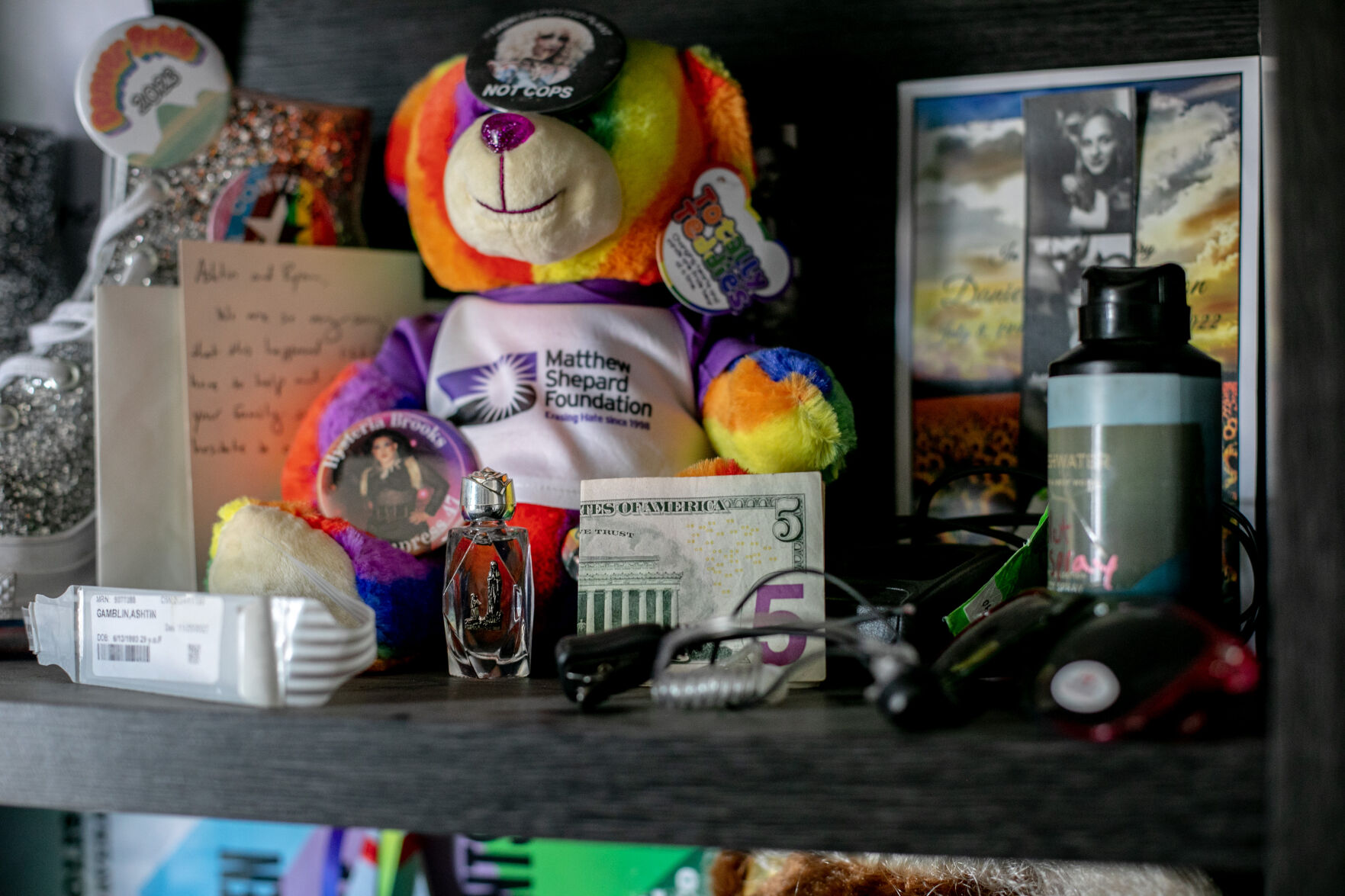 Mementos on Ashtin Gamblin’s “rainbow shelf” include holy water gifted to her from Derrick Rump, a $5 bill Daniel Aston gave her, the wrist band from her first visit to Club Q, hospital bracelet from her stay after the shooting, notes, pins and other miscellaneous things to honor the loved ones she lost and the community she found through the club. (Parker Seibold, the gazette)