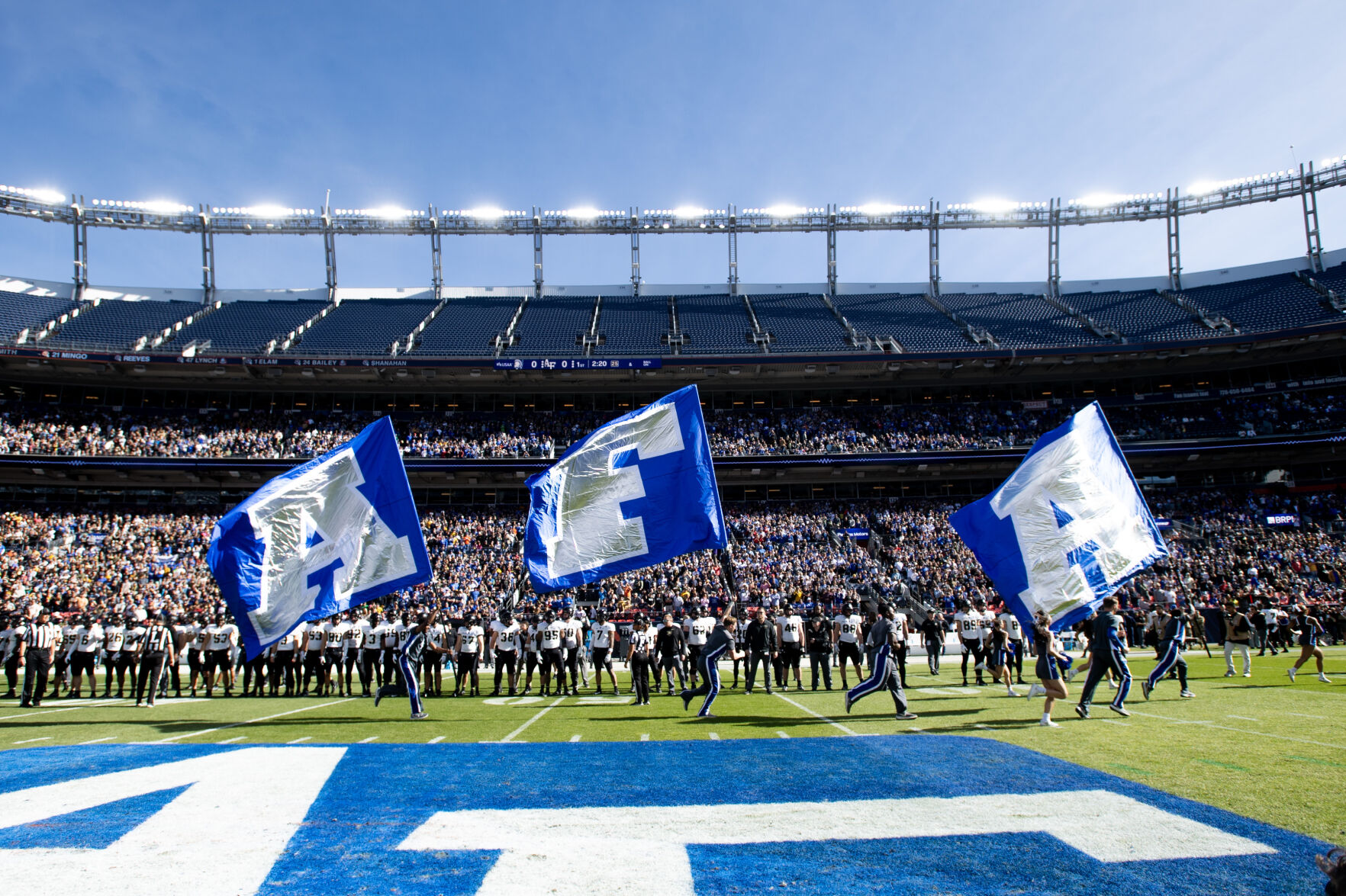 Members of the Air Force Academy cheerleading team run the field with Air Force flags before their game Nov. 4 against Army in Denver. (Parker Seibold, The Gazette)