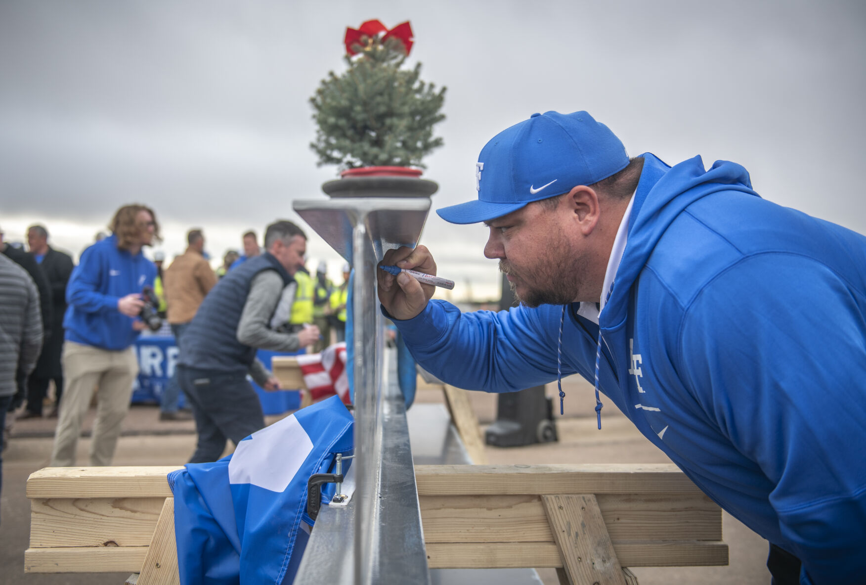 Air Force Academy assistant track and field coach Kyle Lillie takes his turn to sign the final beam of the East Club at Falcon Stadium at Air Force Academy on Friday, December 8, 2023. Lillie is excited as the addition will make the stadium space and amenities competitive with many of the other ‘big schools.’ (Gabi Broekema)