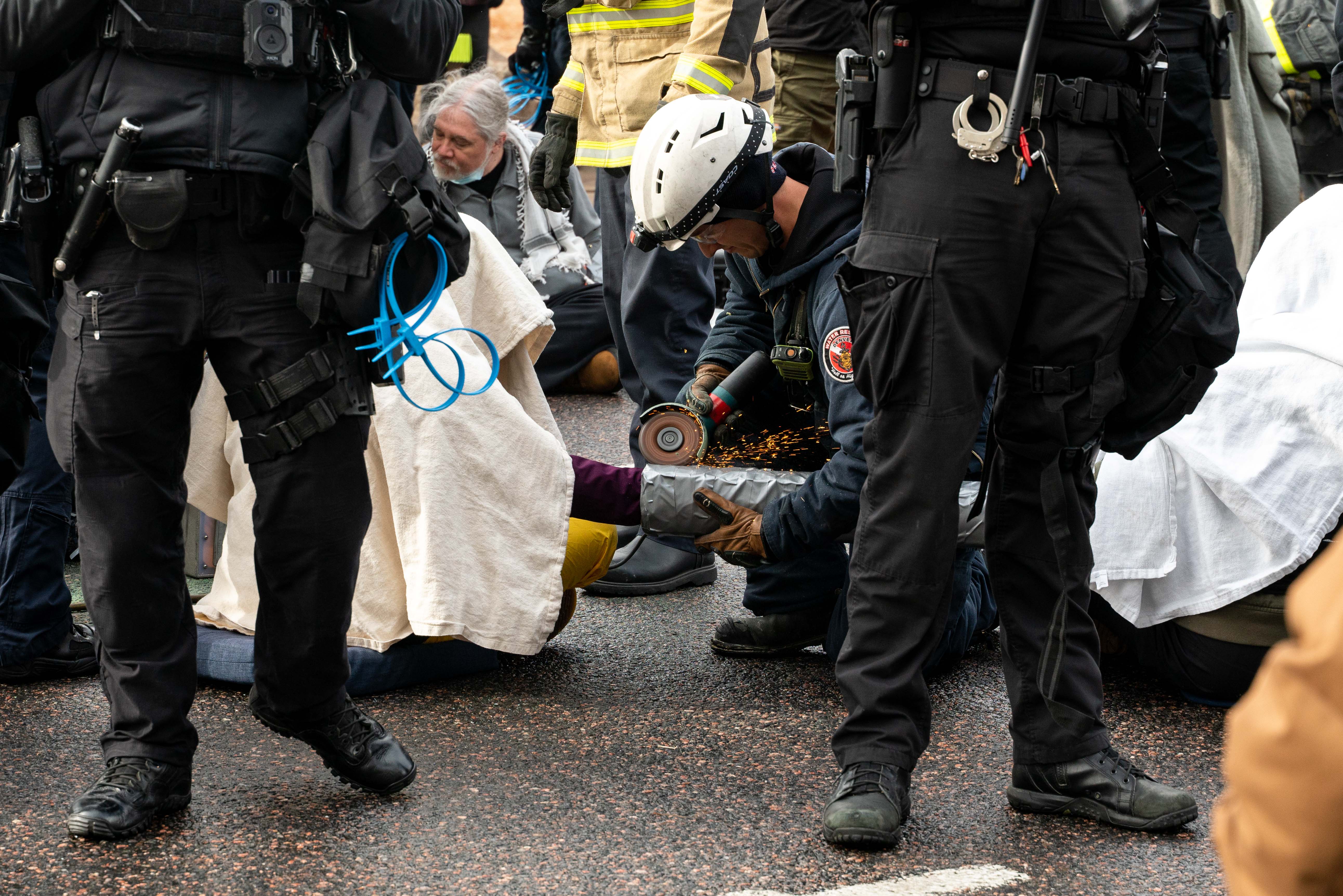 A police officer uses a saw to separate pro-Palestinian activists who chained their arms together using tubes and cement on Sunday, Dec. 3, in Denver. (PHOTO: Jewish Voice for Peace) (genna)