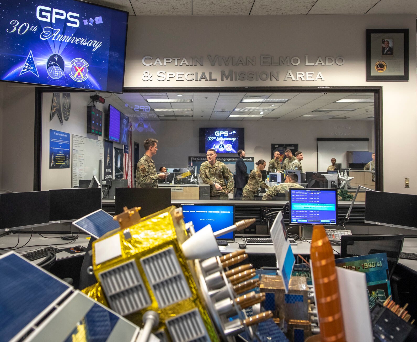 Lead vehicle systems officer Ryan Bonacci speaks with Brandon Mersich at the 2nd Space Operations Squadron, where satellite operators control GPS satellites inside Schriever Space Force Base on Saturday. Models of the satellites Space Force already has in orbit sit in the foreground. (Gabi Broekema, the gazette)