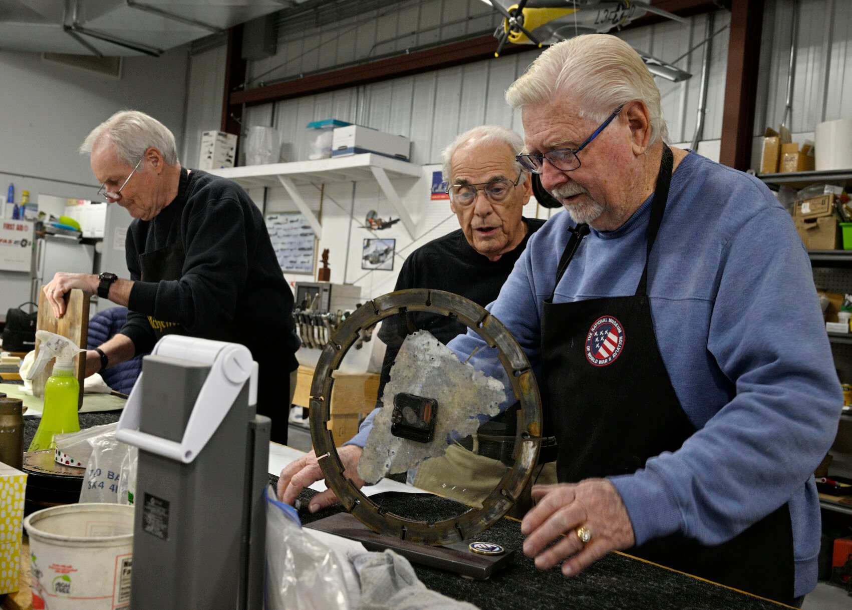 Using some of the discarded aluminum skin of a WWII P-38 Lightning, Larry McManus and Bill Ballard (right to left) collaborate on a clock to be sold as an objet d’art. In the background, Patrick O’Connell works on another project, a weather station using reclaimed airplane parts. (jerilee bennett, the gazette)