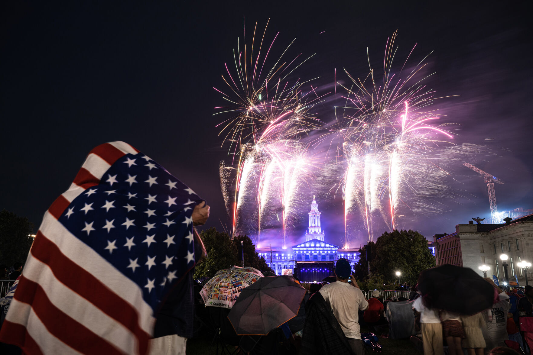 Husband and wife Spike and Jan Lemly attempt to stay dry under an American flag themed blanket during a brief rain shower that fell while fireworks illuminated the sky above the Denver City & County Building at the city’s Independence Eve celebration on Monday, July 3, 2023, in Civic Center Park in Denver. (Timothy Hurst/Denver Gazette) (TimHursttim.hurst@gazette.comhttps://secure.gravatar.com/avatar/aca82bd62b4ee425c598527cd6faa1b1?d=mm&r=g)