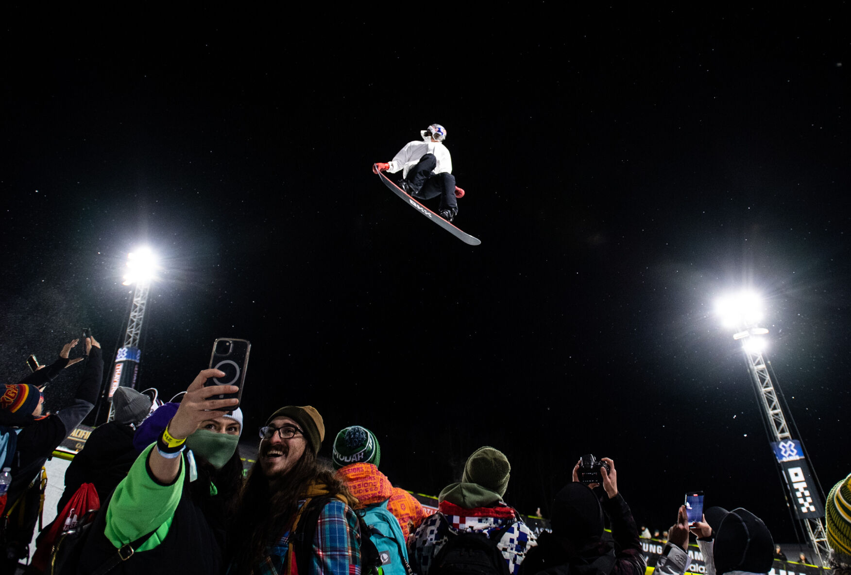 A couple takes a selfie as Snowboard SuperPipe gold medalist Scotty James flies overhead during the finals on day 1 of the X Games Aspen 2024 on January 26, 2024 in Aspen, Colo. (Parker Seibold, The Gazette) (Parker Seibold)