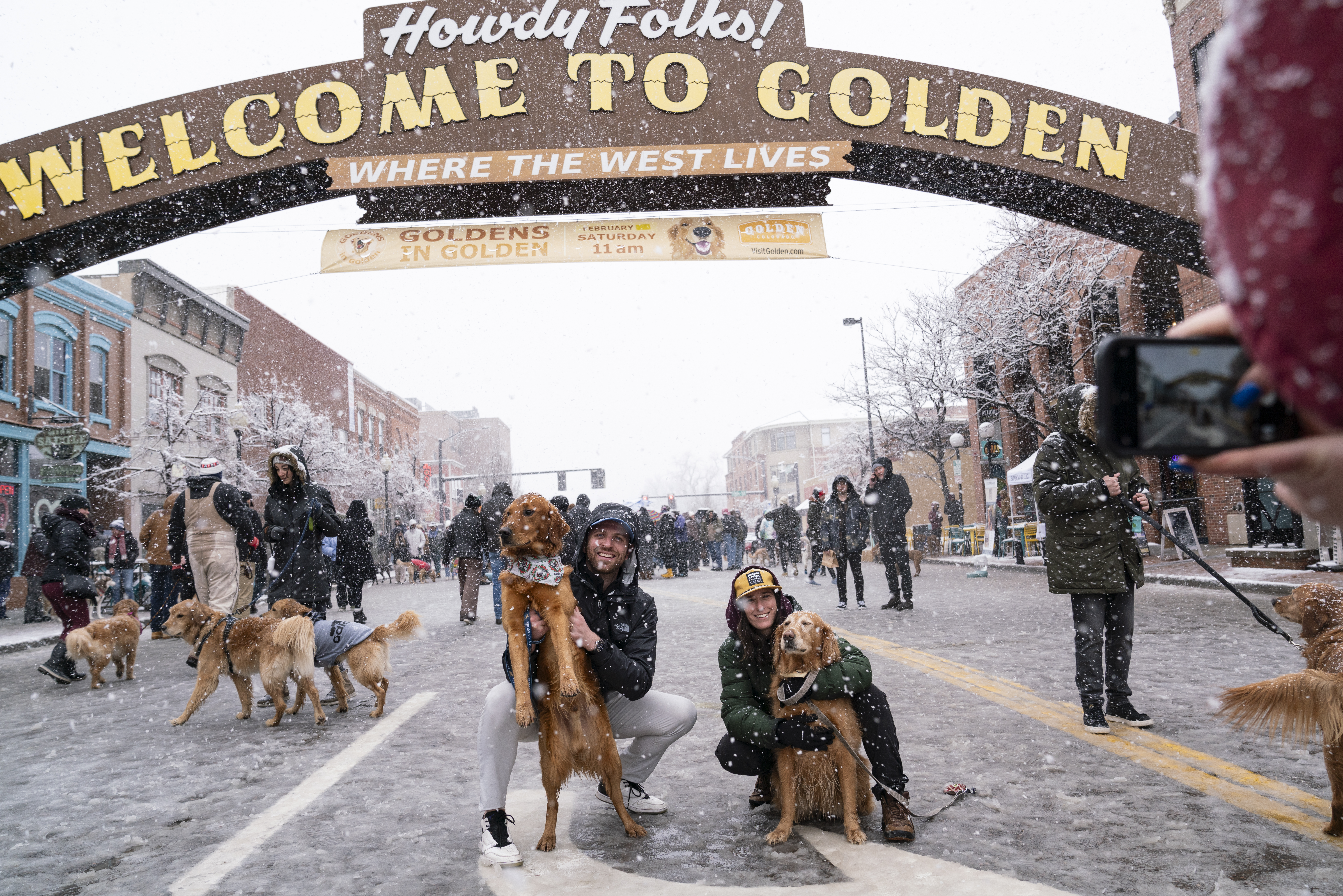 Garrett Reno and Courtney Carr hold Saint and Mae for a photo on Washington Ave. in Golden, Colorado on Saturday, February 3, 2024. The snow didn’t stop owners from bringing their pets to the annual event on National Golden Retriever Day. (Rebecca Slezak)