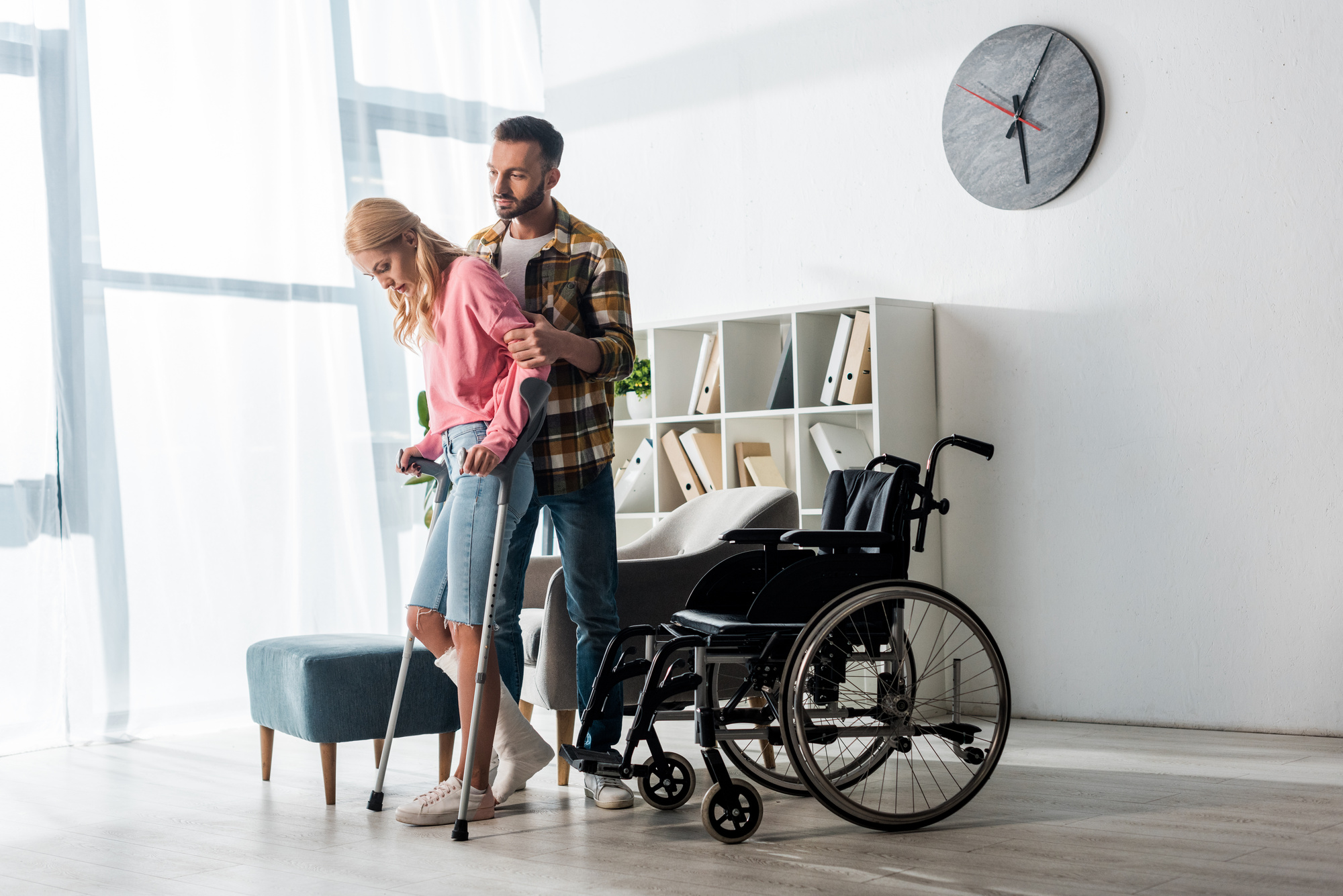 Wheelchair near injured woman holding crutches while standing with man (LIGHTFIELD STUDIOS - stock.adobe.com)