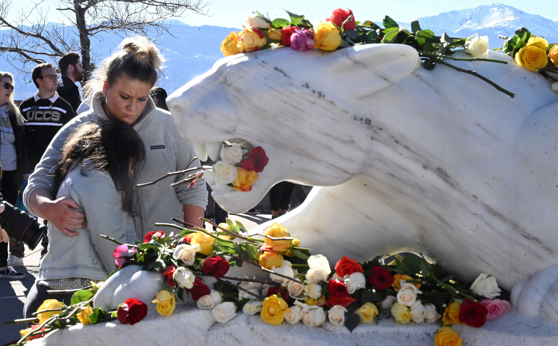 The mountain lion statue at the heart of the UCCS campus was draped in flowers after a Healing Walk for the deaths that happened on campus last week. Student Bella Brooker hugs Sarah Wrubel after the walk on Monday, Feb. 19, 2024. Two people were shot and killed in the dorms last Friday. A suspect was arrested Monday. Also, a student suddenly died from a medical issue several days before the murders. (Photo by Jerilee Bennett, The Gazette)