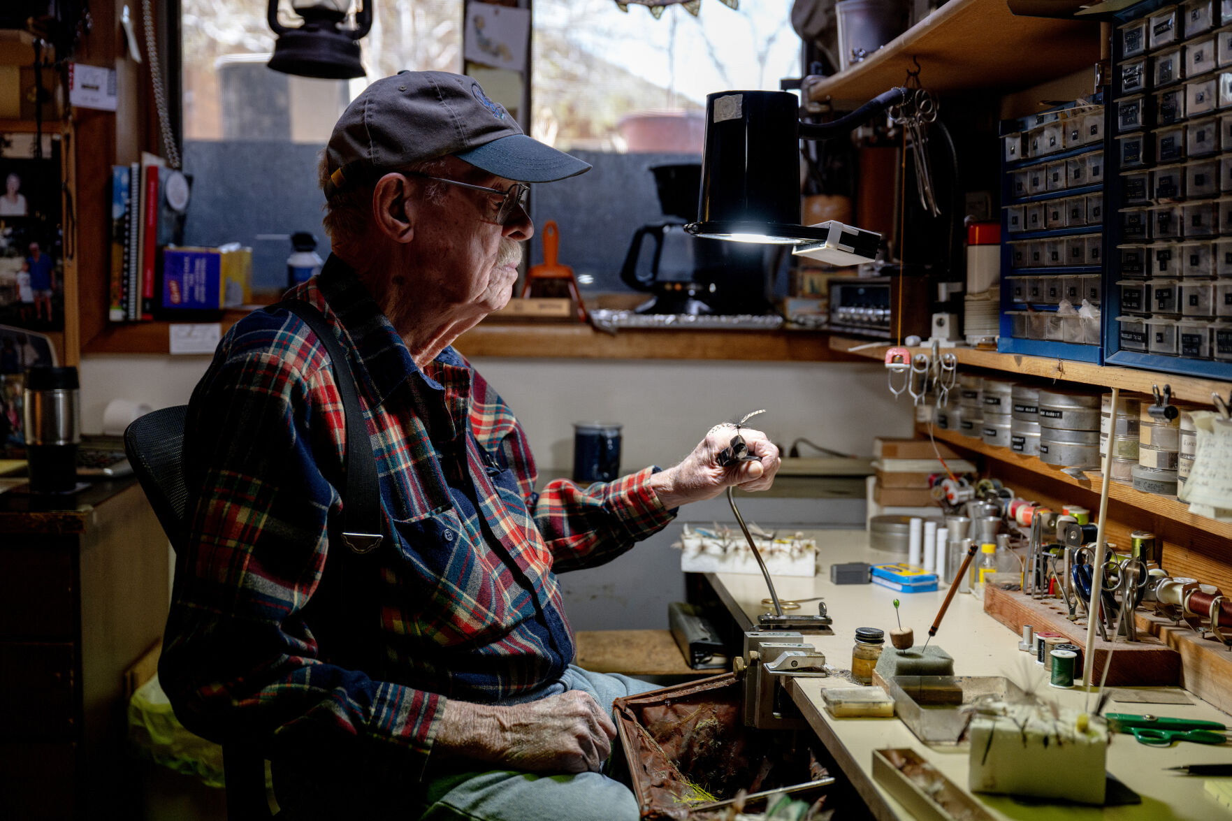 A.K. Best inspects a dragonfly fishing fly as he sits for a portrait last month at the workbench where he spent 40-plus years tying flies 2024, in Boulder. Best is a legend in the fly fishing world for tying flies. (Parker Seibold, the gazette)