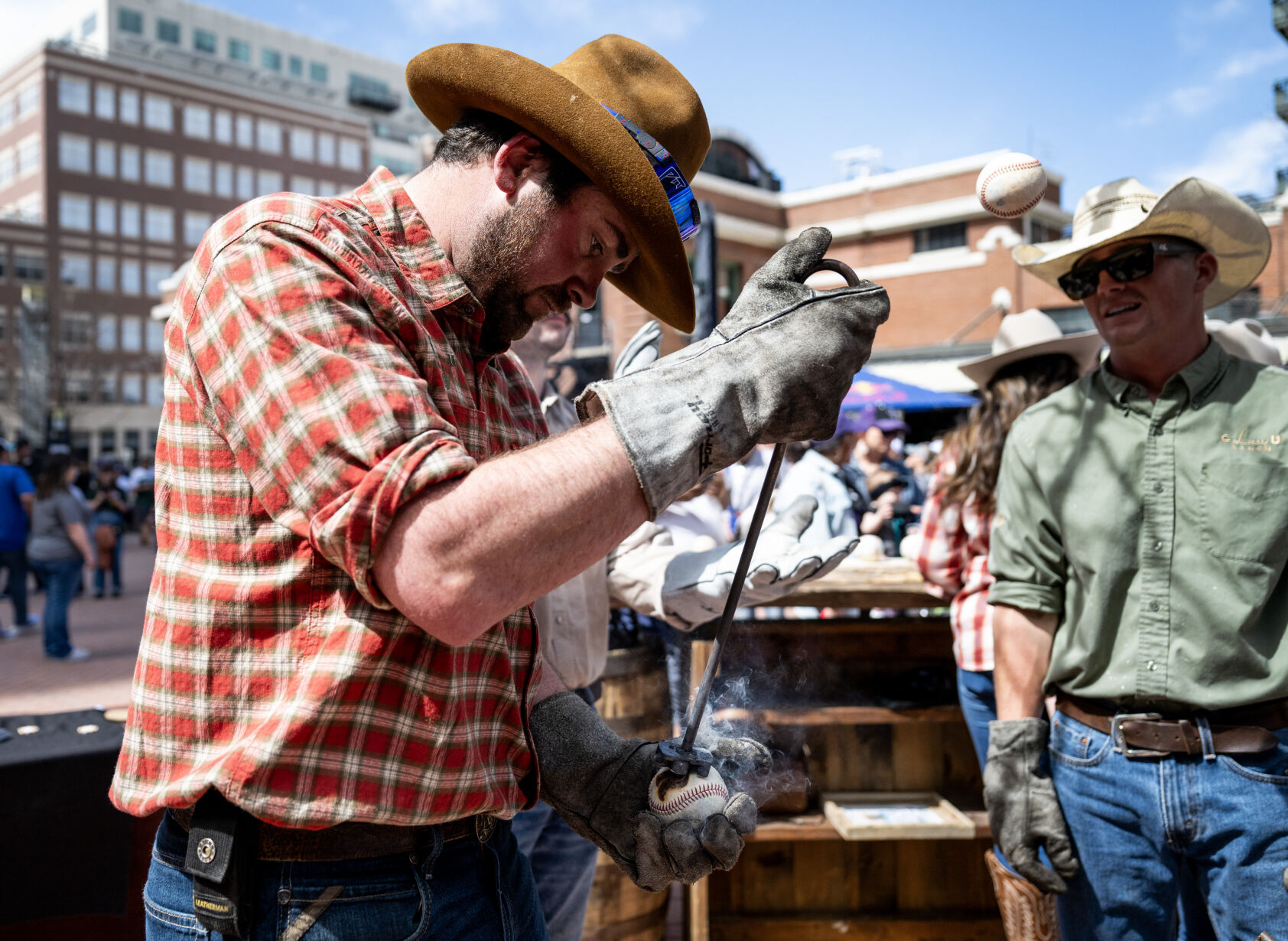 Dael Moulton from C Lazy U Ranch brands a Colorado Rockies logo onto a baseball for a fan at McGregor Square before the home opener at Coors Field, Friday, April 5, 2024, in Denver, Colo. (Parker Seibold, The Gazette) (Parker Seibold)