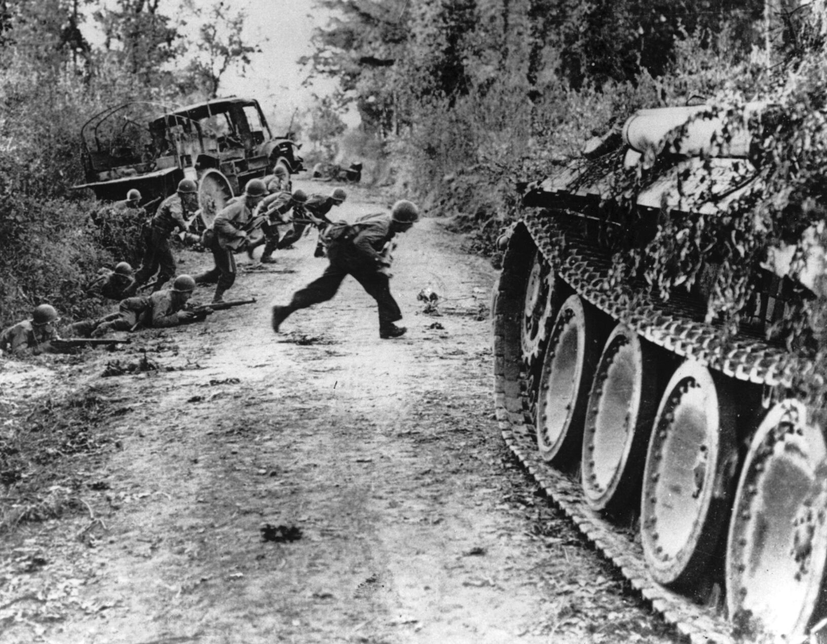 FILE — During the Allied invasion of the Normandy region in France, American soldiers race across a dirt road under enemy fire, near St. Lo, in July 1944. France is getting ready to show its gratitude towards World War II veterans who will come, many for the last time, on Normandy beaches for D-Day ceremonies that will come as part of a series of major commemorations this year and next marking eight decades since the defeat of the Nazis. (Pool via AP, File) (POOL)