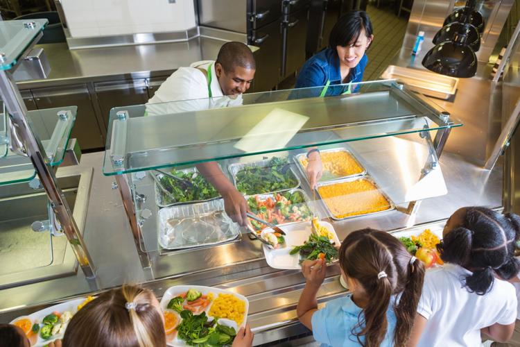 Cafeteria worker serving trays of food to children school lunches