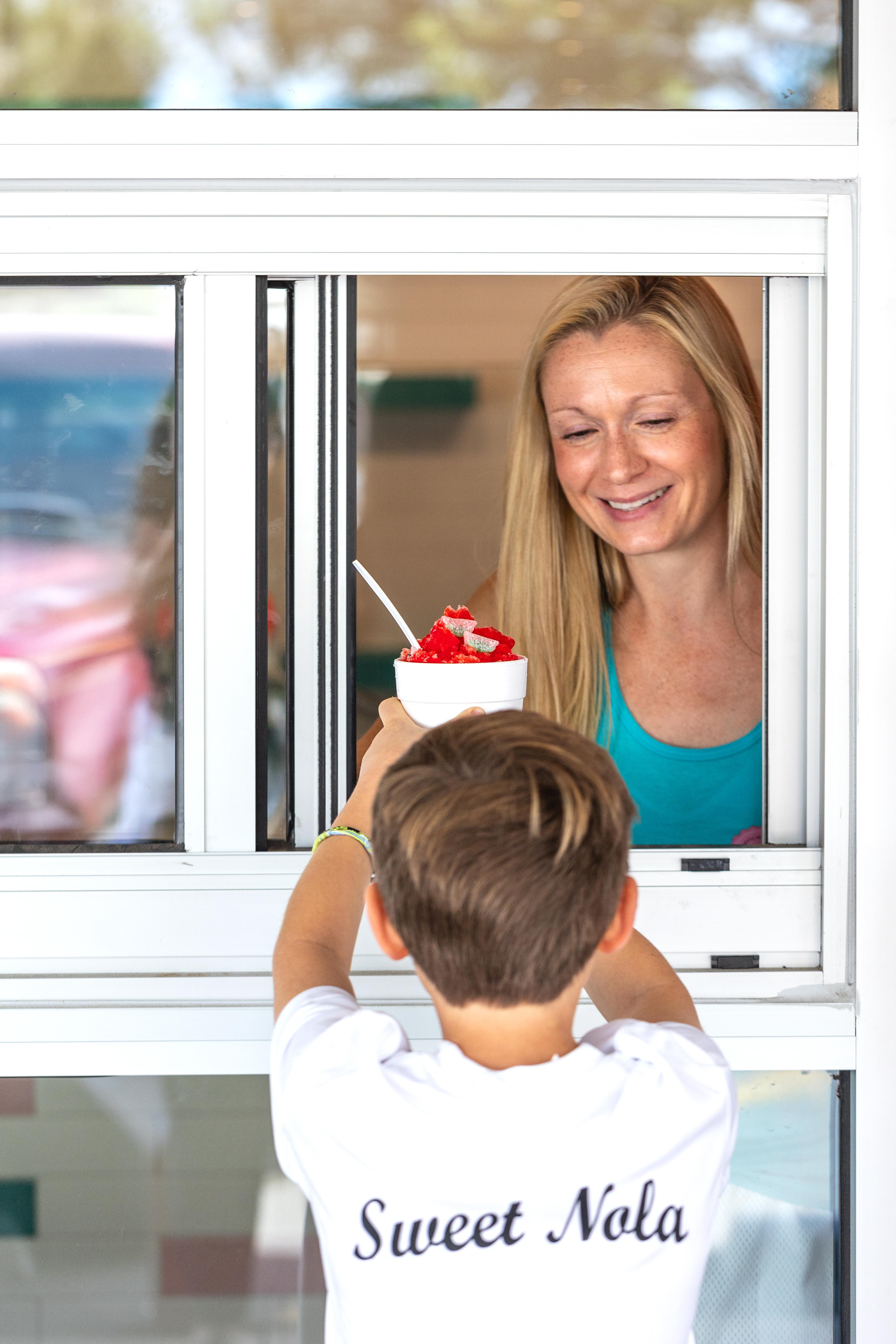 Sweet NOLA Snoballs, which serves finely shaved ice cones with syrup made famous in New Orleans, opened Friday at 916 Jersey Street, Denver. Owner Lara Stepneski-Mintz shown serving her son through the shop's walk-up window. (Courtesy photo, Cognoscenti Creative)
