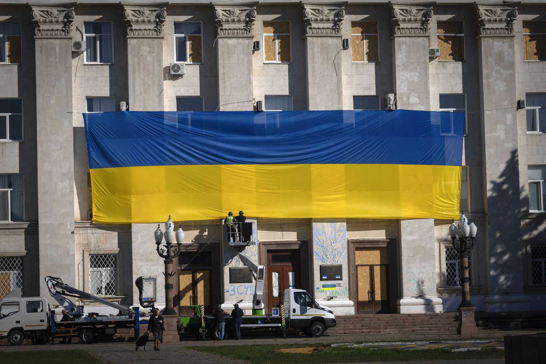 Municipal workers wearing protective vests and helmets decorate the wall of the regional administration building with a huge national flag Friday to mark one year since the Ukrainian troops cleared the city from the Russian army in Kherson, Ukraine. (associated press file)