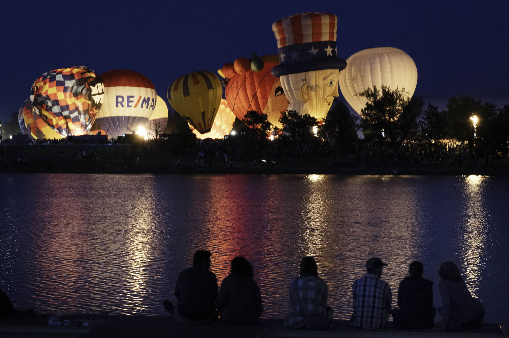 Balloons are reflected in the waters of Prospect Lake during the balloon glow of the Colorado Springs Labor Day Lift Off on Sunday, Sept. 1, 2024.