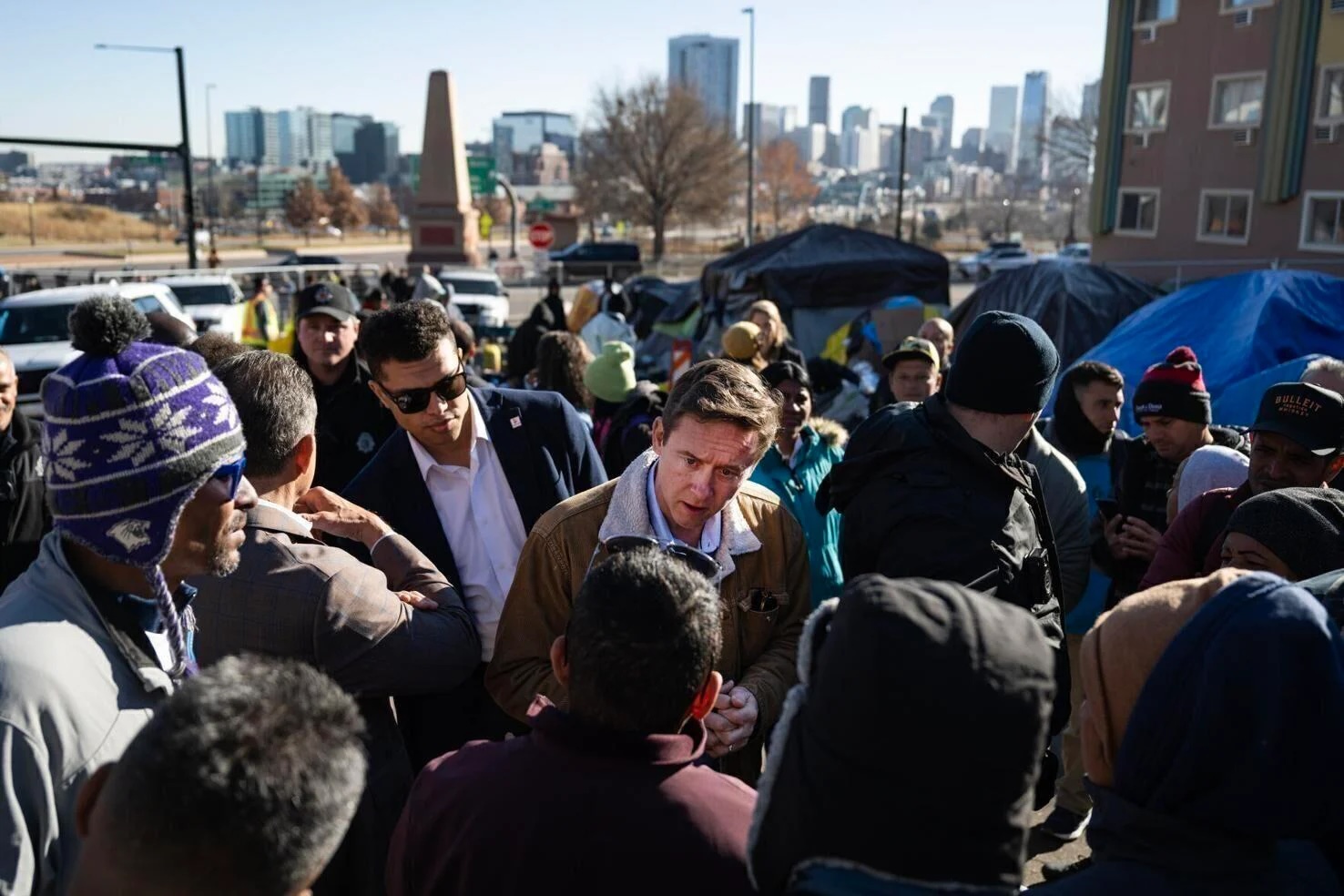 Denver Mayor Mike Johnston, center, talks with immigrants during an encampment sweep last January. (Gazette file)