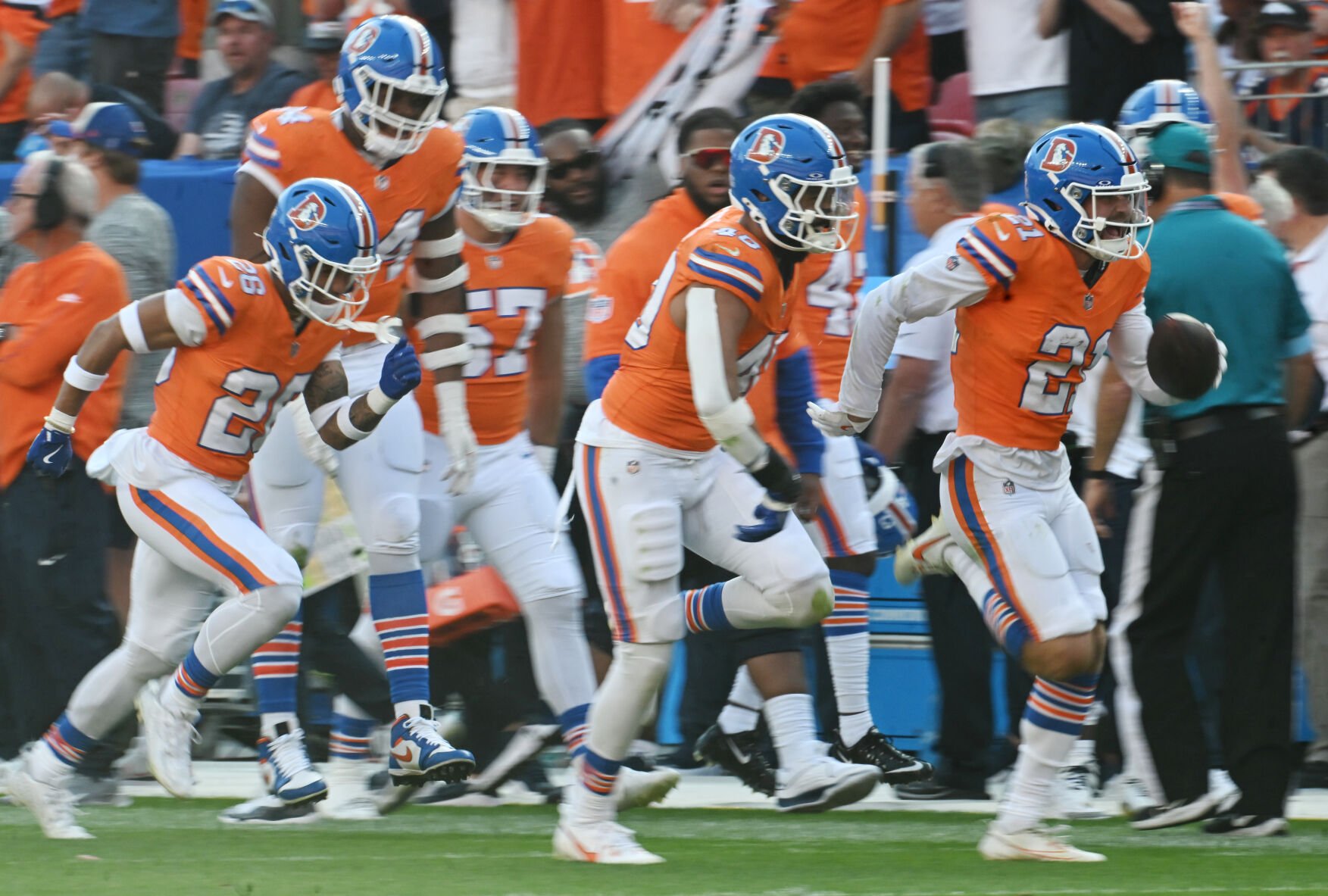 Denver Broncos cornerback Riley Moss (21) is escorted down the field by teammates after making an interception for a pick six during the fourth quarter of a game at Empower Field at Mile High on Sunday, Oct. 6, 2024. The Broncos won the game 34-18. (Jerilee Bennett, The Gazette)