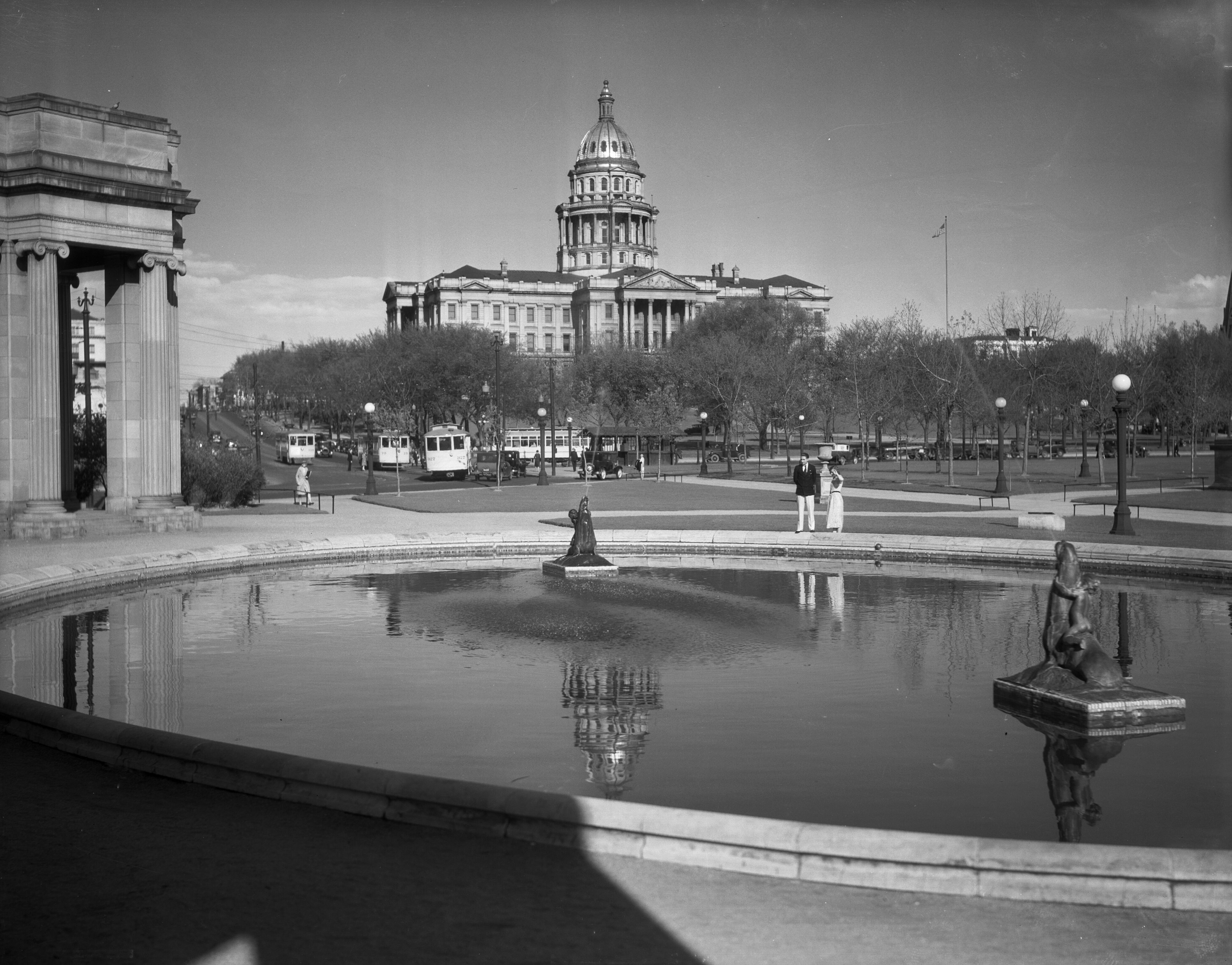 View of the Colorado State Capitol building, Denver, Colorado; shows people standing by the Civic Center reflecting pool and colonnade, trees, and streetcars of the Denver Tramway Company. Photo taken in roughly 1929 (Denver Public Library Archive) (Courtesy photo, Denver Public Library Archive)