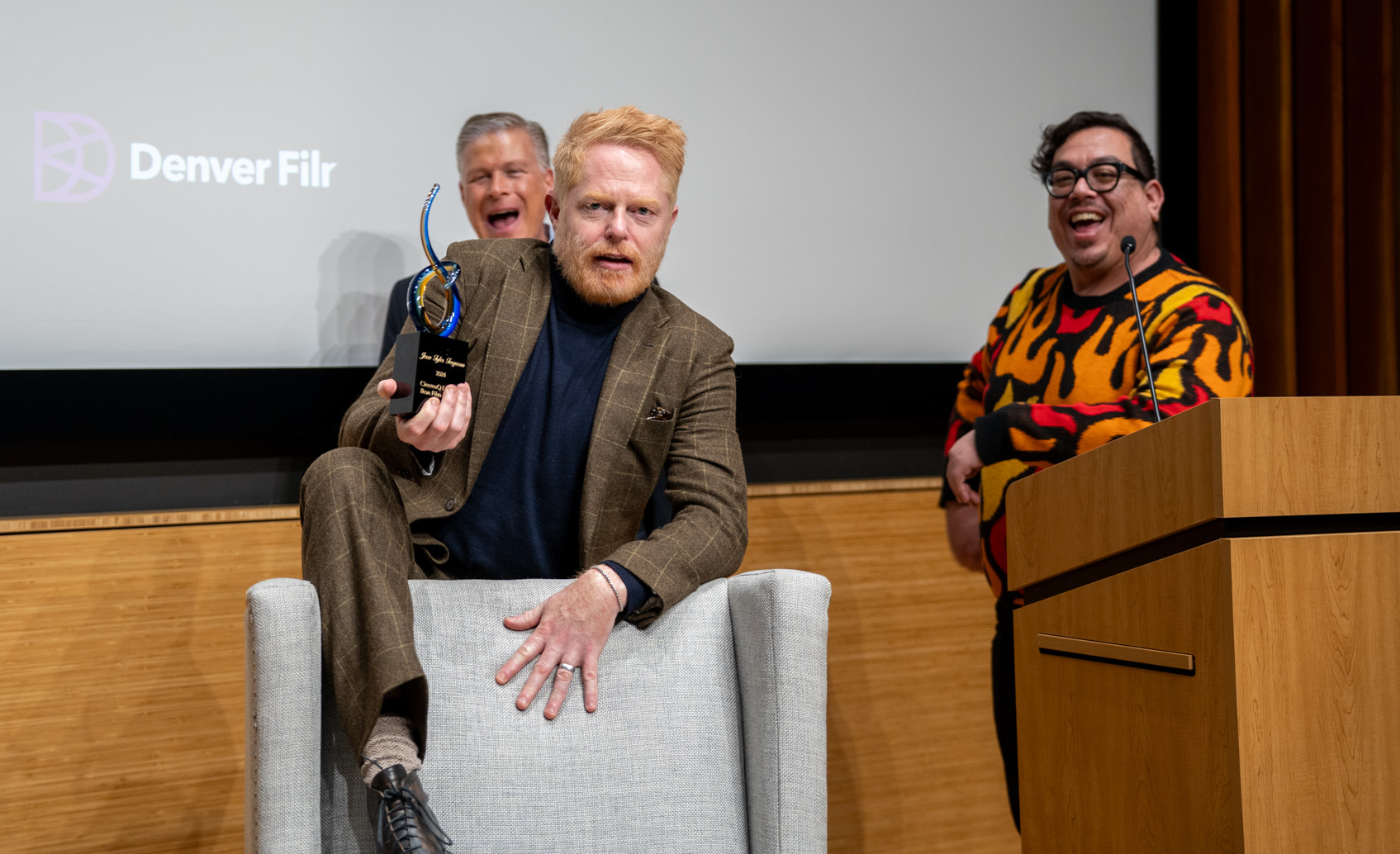 Jesse Tyler Ferguson has some fun accepting Denver Film's 2024 CinemaQ LaBahn Ikon Film Award, which celebrates cinematic excellence within the LGBTQ community. Behind him are award namesake Will LaBahn, left, and CinemaQ founder Keith Garcia on Nov. 7, 2024, at the Denver Botanic Gardens. (BEAU NGU/DENVER FILM)