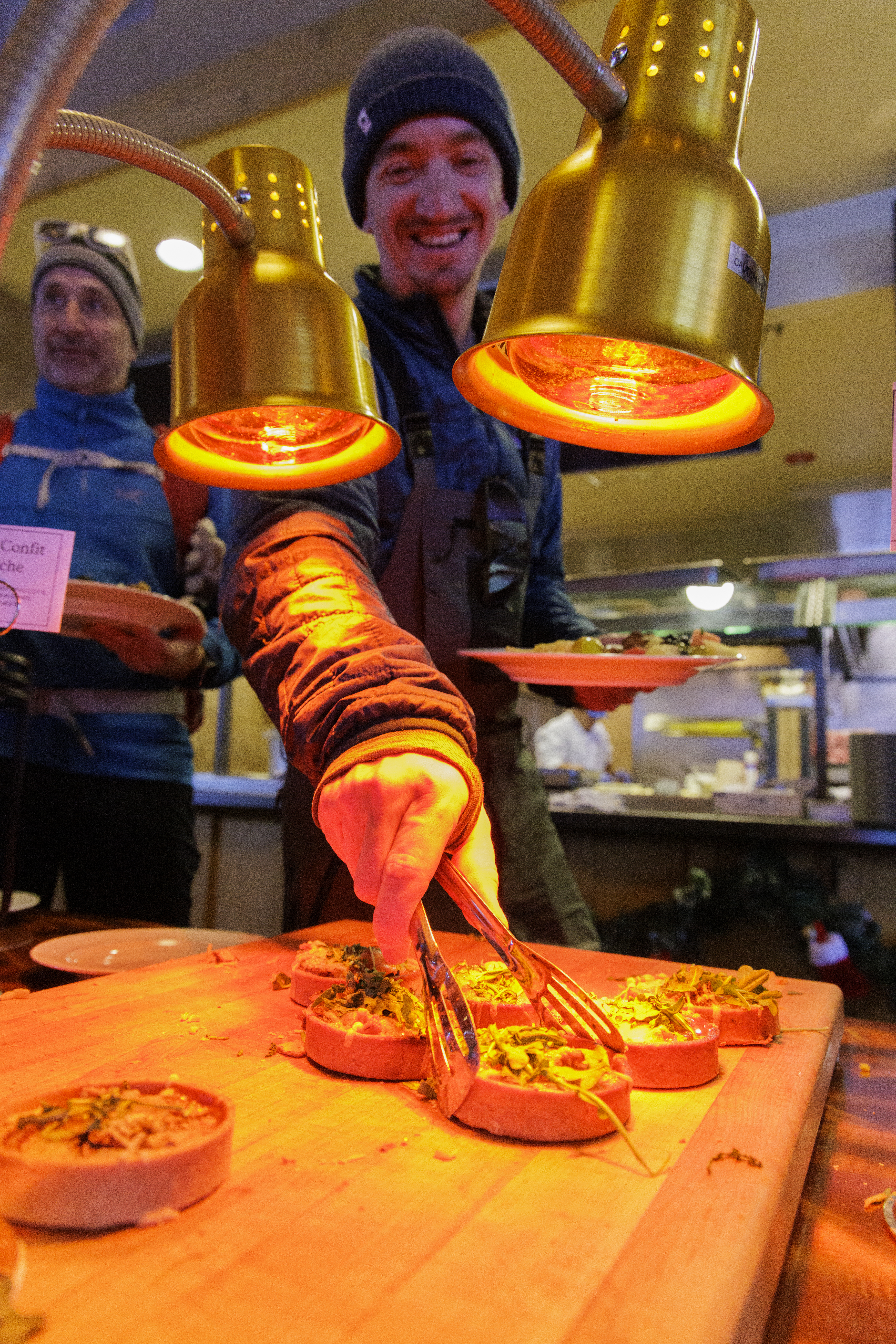 A breakfast meal sits under a heat lamp while a man picks up the food with tongs during an Uphill & Chill Breakfast Friday, Dec. 6, 2024 at Arapahoe Basin Ski Area. (Courtesy photo, Lucas Herbert, Arapahoe Basin Ski Area)