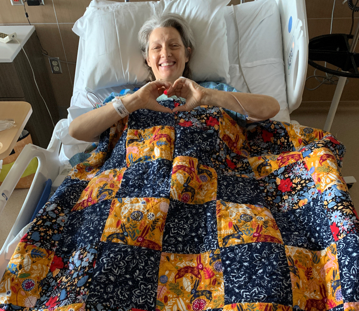 Mare Trevathan recuperates at the Anschutz Medical Center on April 3, 2024, after donating her kidney to Lee Anderson, who is a friend – but Trevathan said that after learning more about living organ donation, she would have happily given one up to a stranger. More than 800,000 Americans are in varying stages of renal failure. She is draped by a quilt made by her sister-in-law, Sherry Klander. (COURTESY MARE TREVATHAN)