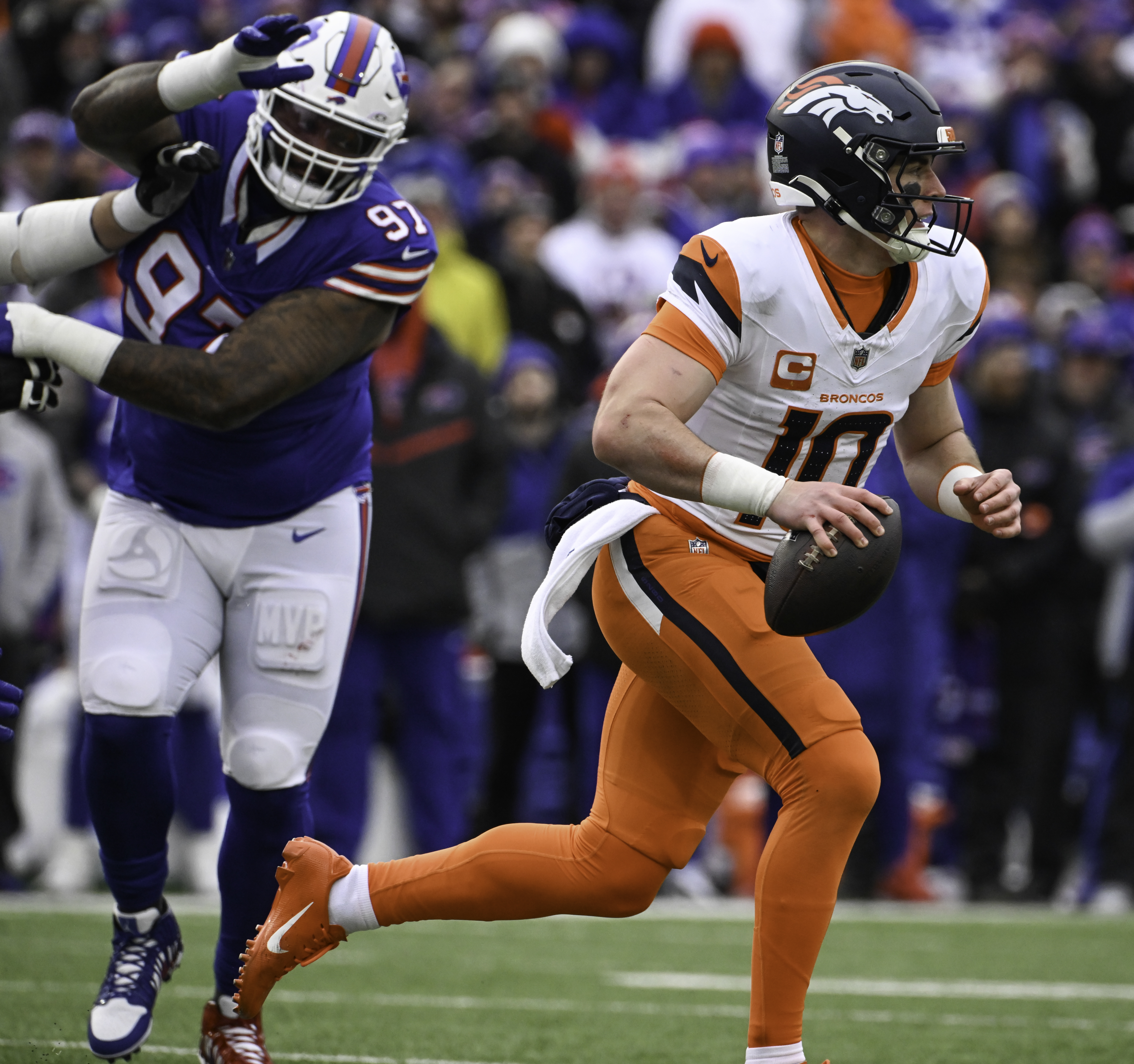 Denver Broncos quarterback Bo Nix (10) runs with the ball while being pursued by Buffalo Bills defensive tackle Jordan Phillips (97) during the second quarter of the wild card playoff game at Highmark Stadium in Buffalo on Sunday, Jan. 12, 2025. The Broncos lost 31-7. (Jerilee Bennett,The Gazette)