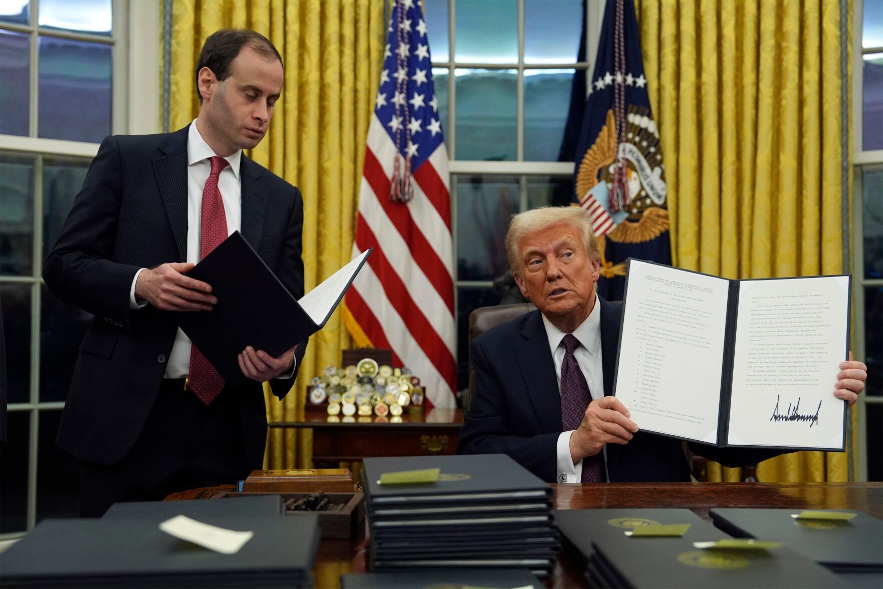 President Donald Trump holds up an executive order commuting sentences for people convicted of Jan. 6 offenses in the Oval Office of the White House on Monday. (The Associated Press)