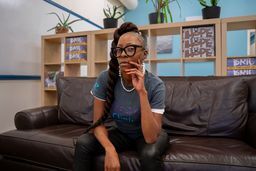 Erica Green, who manages the At-Risk Intervention and Mentoring program, or AIM, sits on a couch in the new REACH Clinic in Denver’s Five Points neighborhood. Green came to this work after her family’s own experience with gun violence: “I feel very blessed to be able to show up for my community this way.” (Stephanie Wolf, KFF Health News)