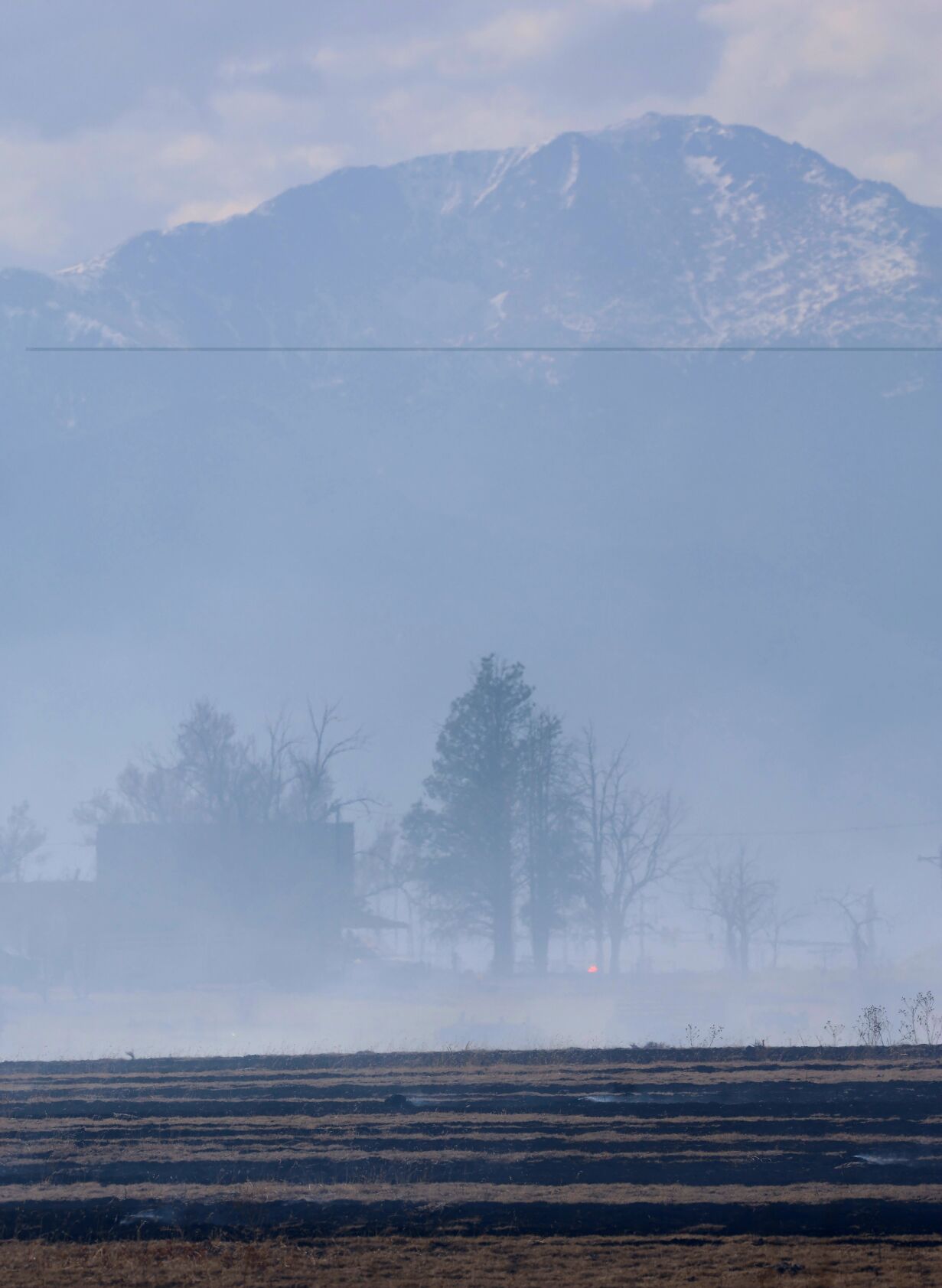 Pikes Peak seen behind a haze of smoke on March 13, 2025, with some of the charred grass from the Meridian Fire seen in the foreground. (Courtesy Milton Mills)