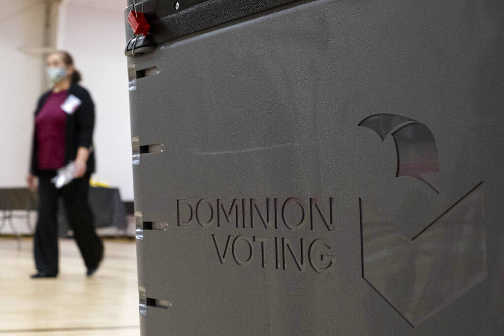 FILE PHOTO: A worker passes a Dominion Voting ballot scanner while setting up a polling location at an elementary school in Gwinnett County, Ga., outside of Atlanta on Monday, Jan. 4, 2021, in advance of two Senate runoff elections. (JoeyBunchjoey.bunch@coloradopolitics.comhttps://secure.gravatar.com/avatar/66505e98f9e3fed10e6a3b9a1fc4ca22?d=mm&r=g)