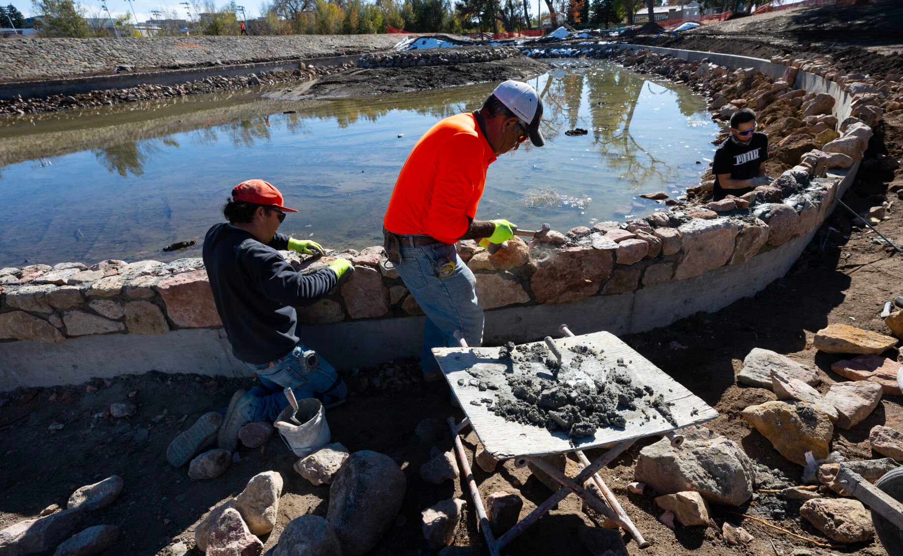 Crispin Rodelas, center, shapes a stone before setting it in place while Anthonio Ortiz, left, and Aron Martinez add the finishing work to the stone wall surrounding Duck Lake in Monument Valley Park Monday, Nov. 18, 2024, in Colorado Springs. (The Gazette, Christian Murdock) (Christian Murdock, The Gazette)
