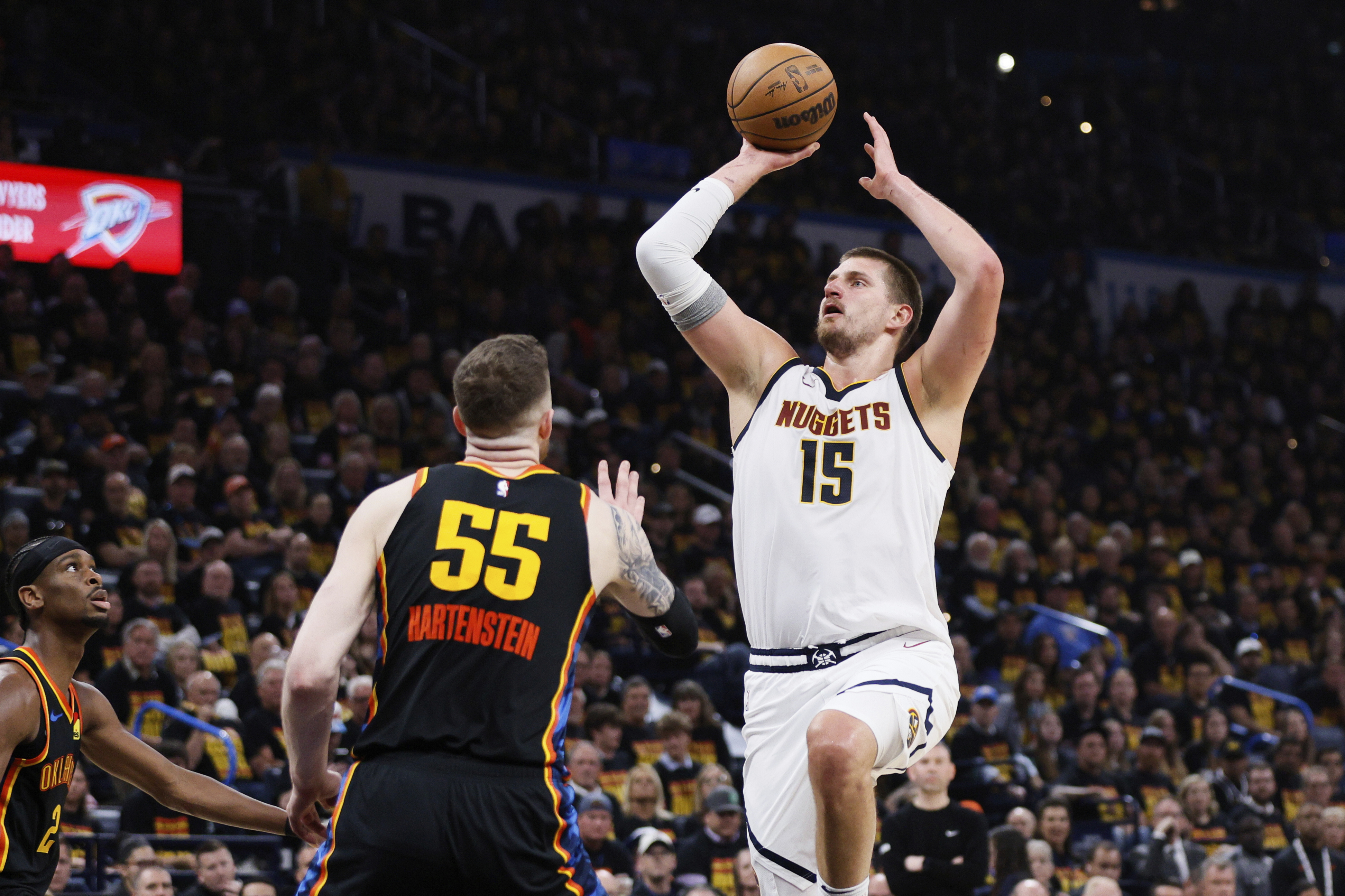 Denver Nuggets center Nikola Jokic (15) shoots over Oklahoma City Thunder's Isaiah Hartenstein (55) and Shai Gilgeous-Alexander, left, in the first half of Game 1 of an NBA basketball second-round playoff series Monday, May 5, 2025, in Oklahoma City. (AP Photo/Nate Billings) (Nate Billings)