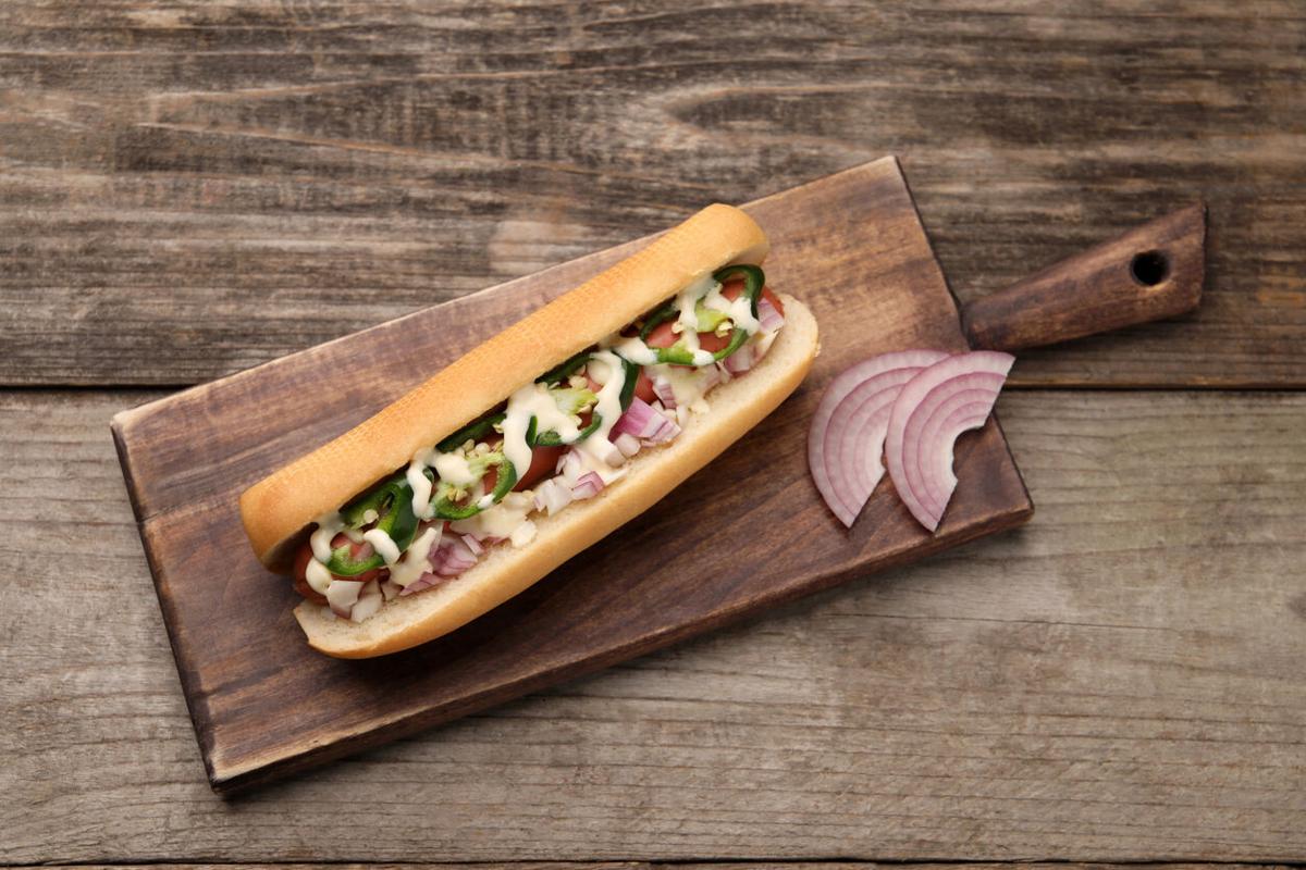 Delicious hot dog with onion, chili pepper and sauce on wooden table, top view