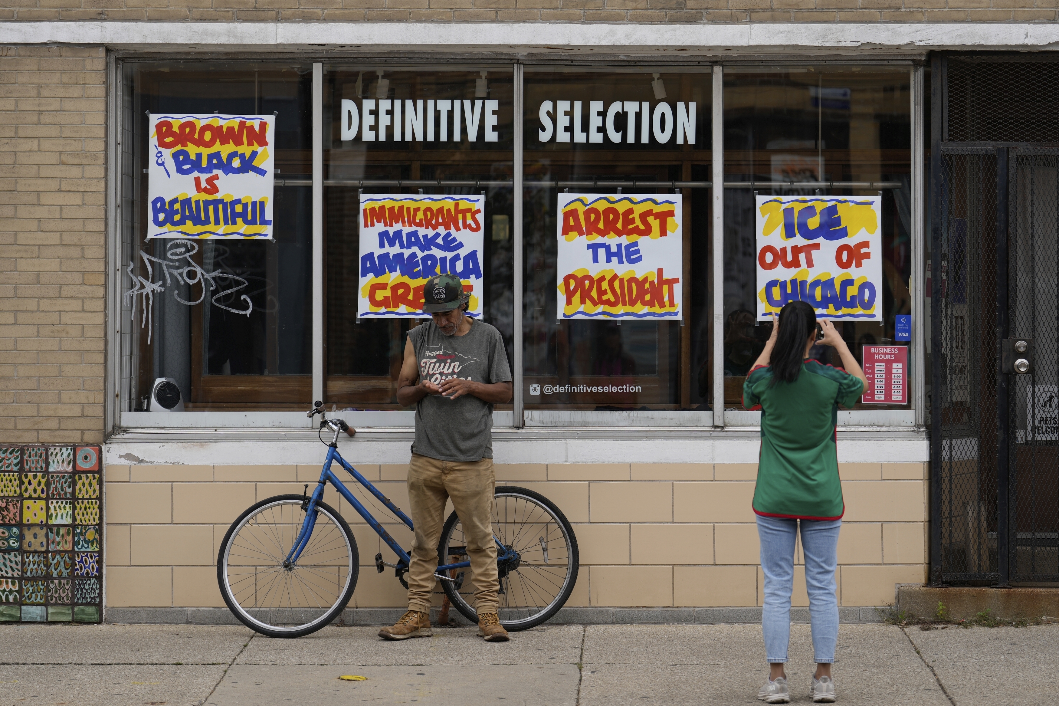People stop to take pictures of signs posted on windows at a clothing store during the 2025 Pilsen Mexican Independence Day parade Saturday, Sept. 6, 2025, in Chicago. (Carolyn Kaster - AP)