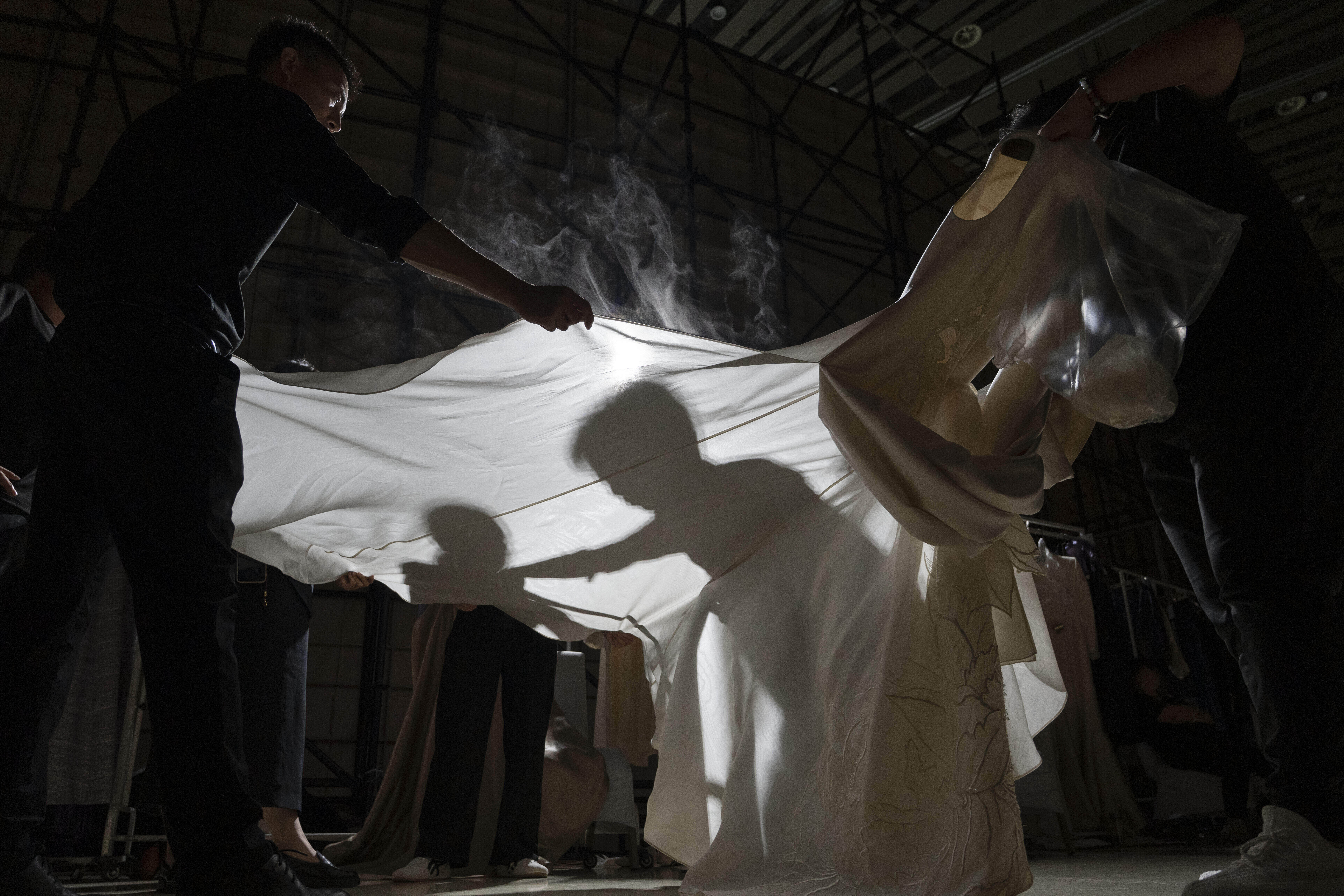 Workers steam press gowns backstage before the Misuity SS2026 China Fashion Week opening show held on the outskirts of Beijing, China, Friday, Sept. 5, 2025. (Ng Han Guan - AP)