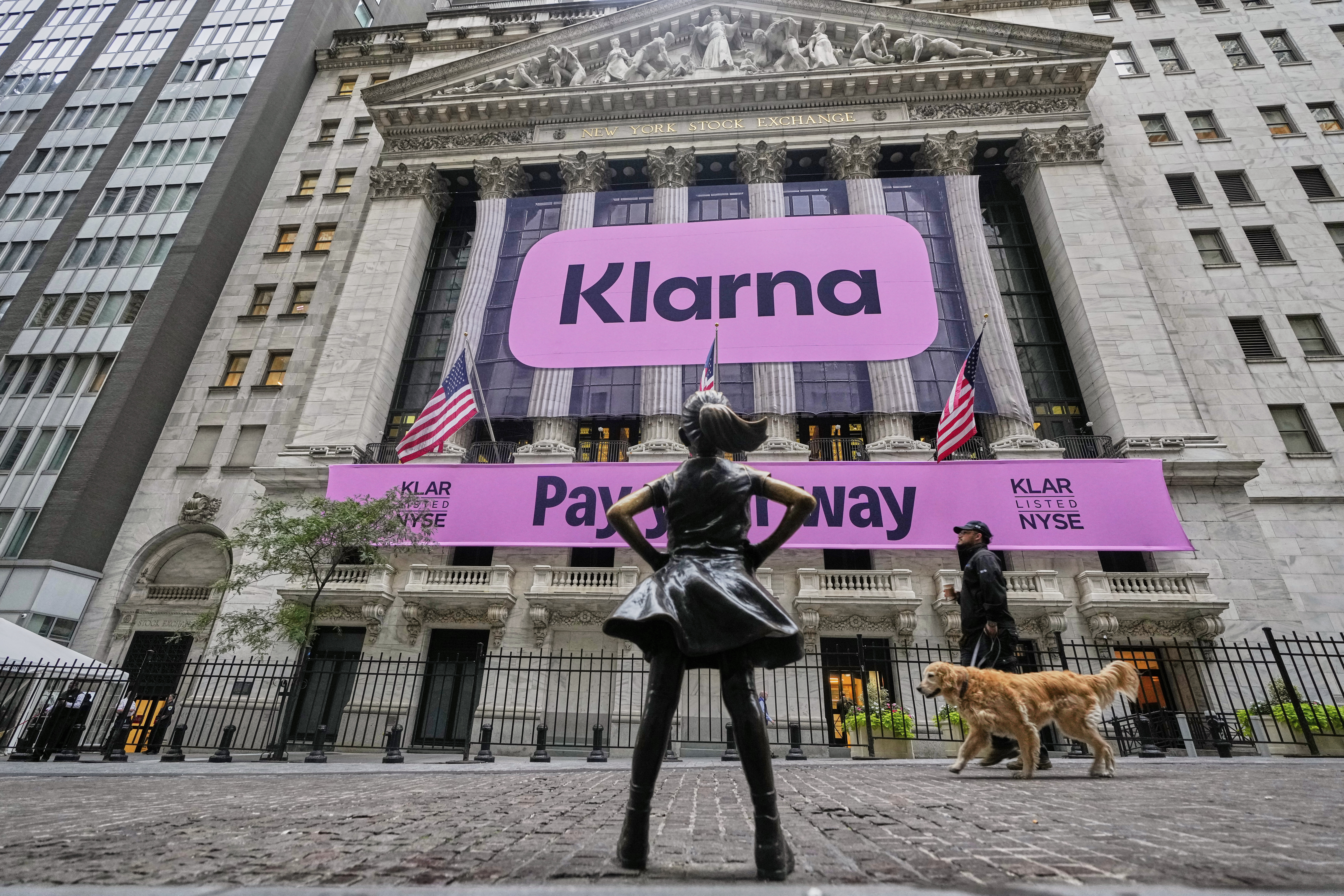 The Fearless Girl statue faces the facade of the New York Stock Exchange that displays signage for Sweden's Klarna, Wednesday, Sept. 10, 2025. (Richard Drew - AP)
