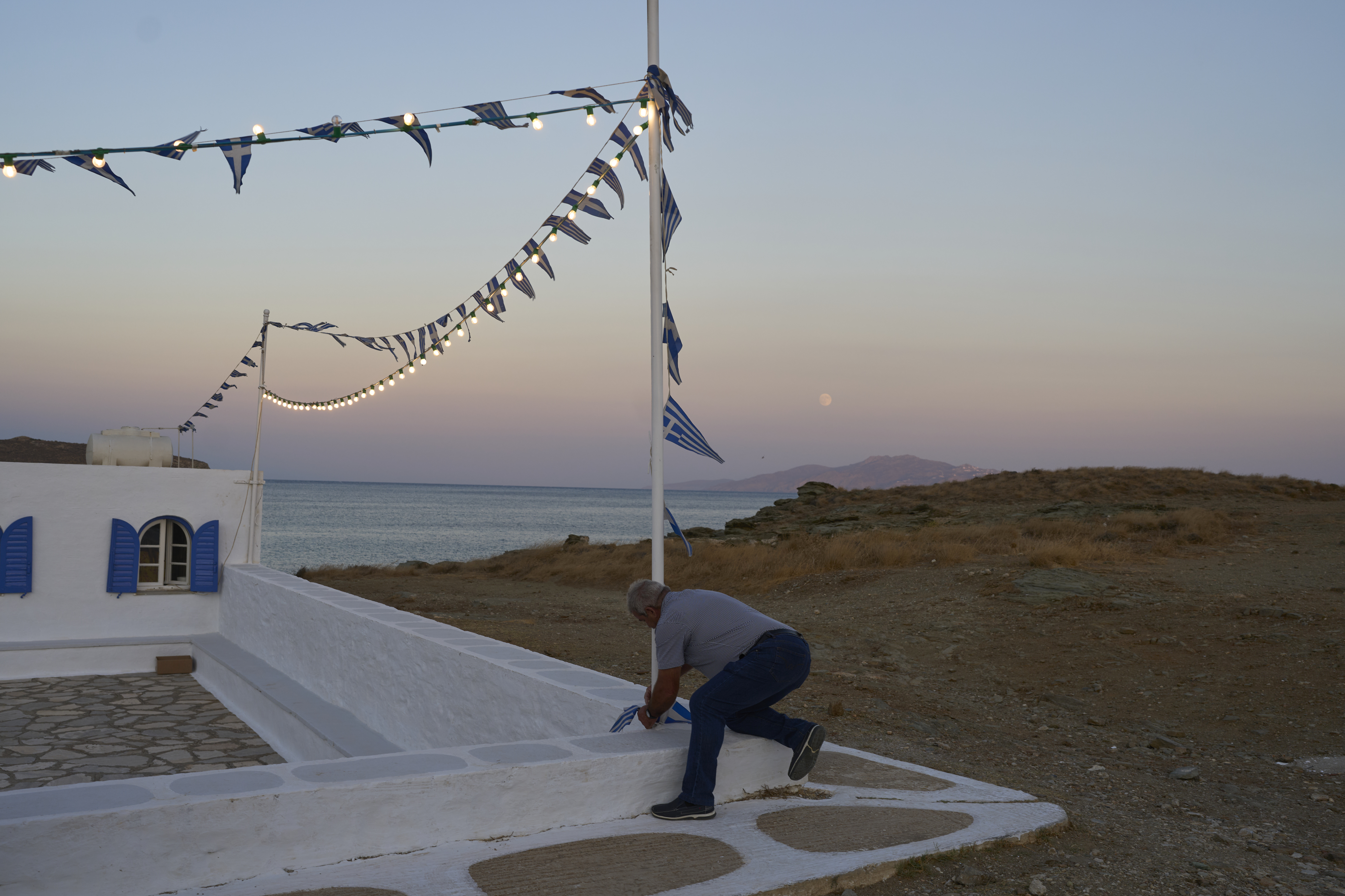 Zerar Delatolas fastens Greek flags to a pole outside the family-owned Agios Sostis chapel during its annual panigiri, on the island of Tinos, Greece, Saturday, Sept. 6, 2025. (Petros Giannakouris - AP)