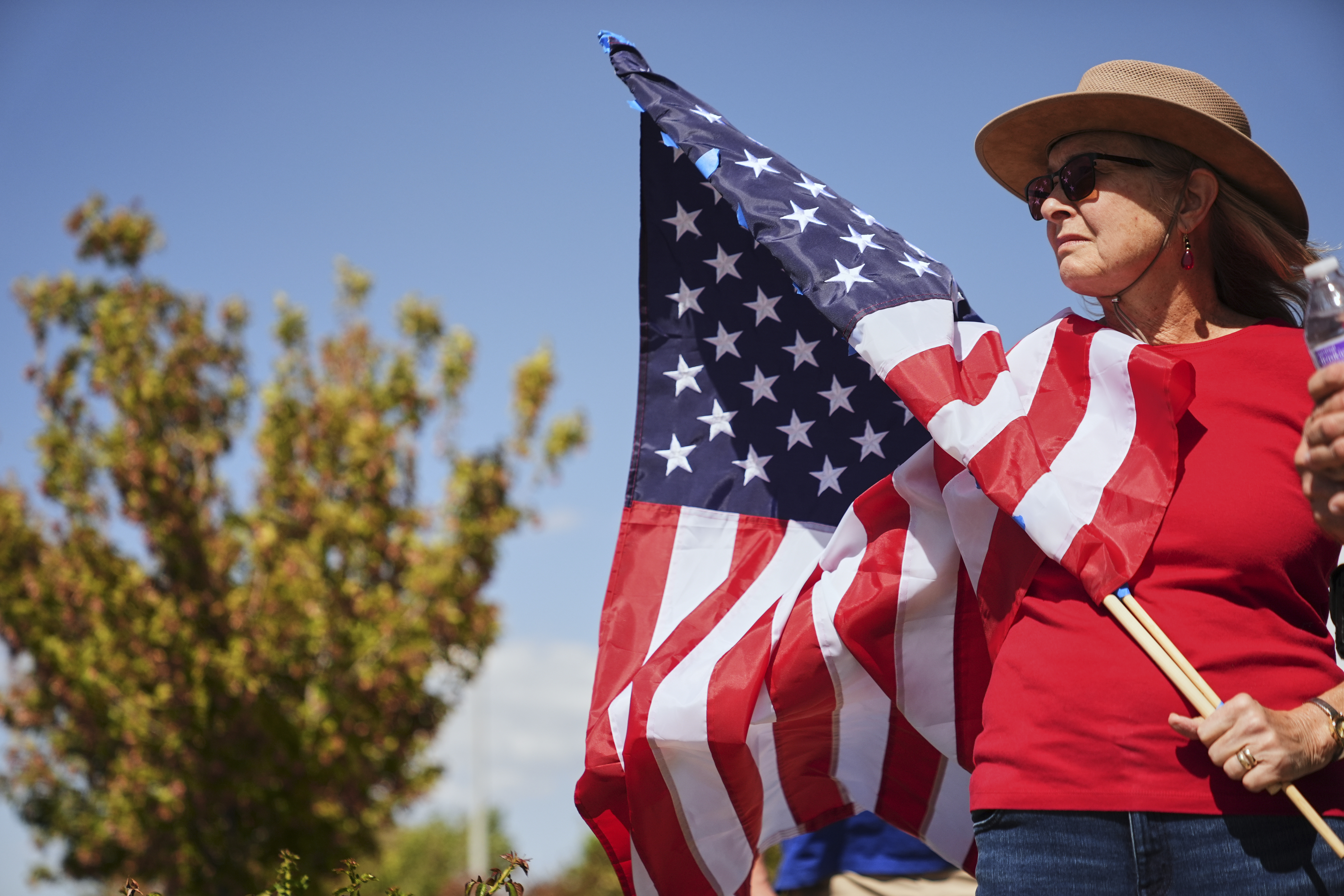A woman holding an American flag stands outside the entrance of the Roland R. Wright Air National Guard Base in Salt Lake City, Thursday, Sept. 11, 2025, where a hearse transporting the remains of Charlie Kirk arrived to be flown in Air Force Two to his home in Arizona. (Lindsey Wasson - AP)