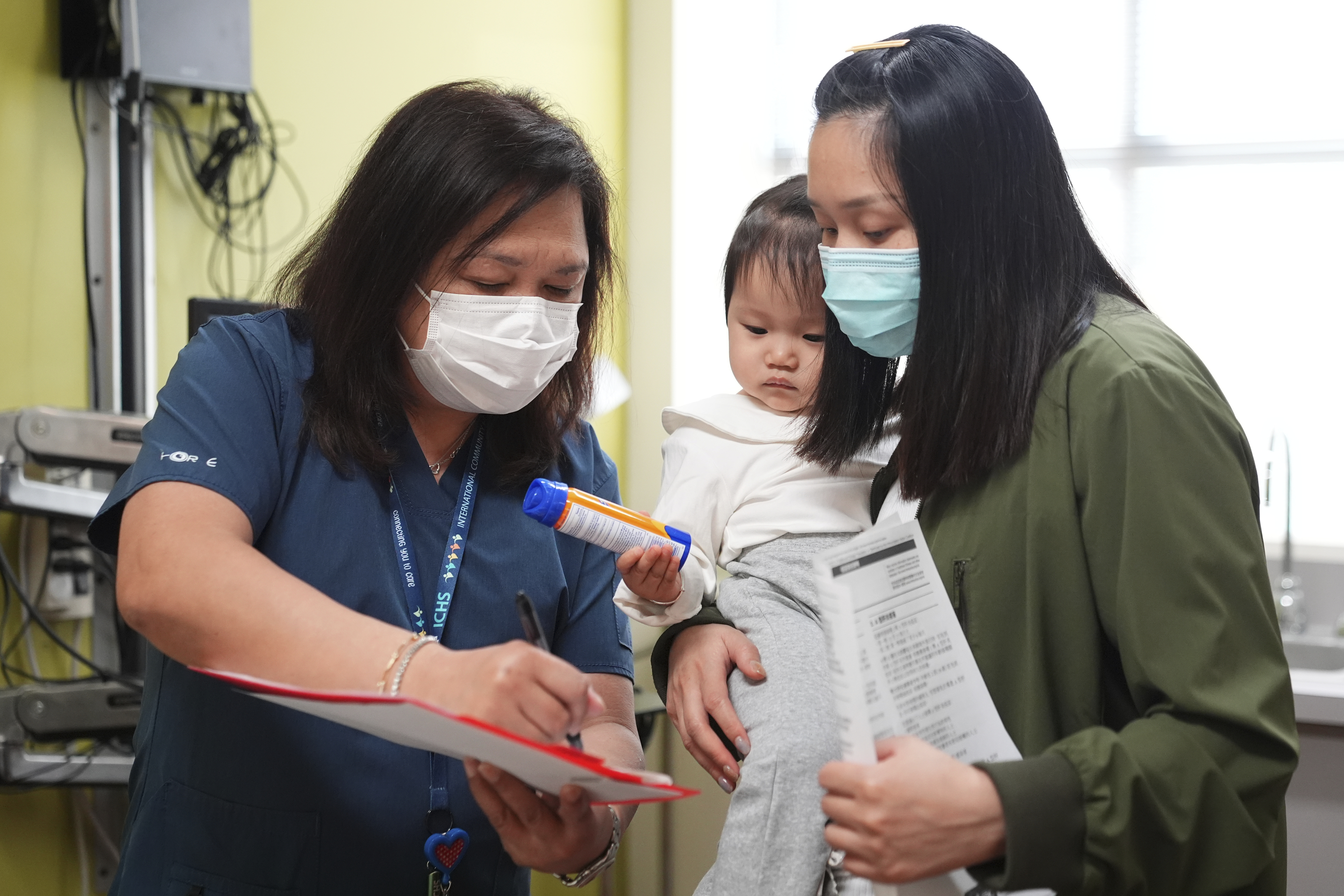 Lead medical assistant Maria Teresa Diocales goes over vaccine information with Huanyu Zhen as her daughter Lena Kuang, 1, looks on at International Community Health Services, Wednesday, Sept. 10, 2025, in Seattle. (Lindsey Wasson - AP)