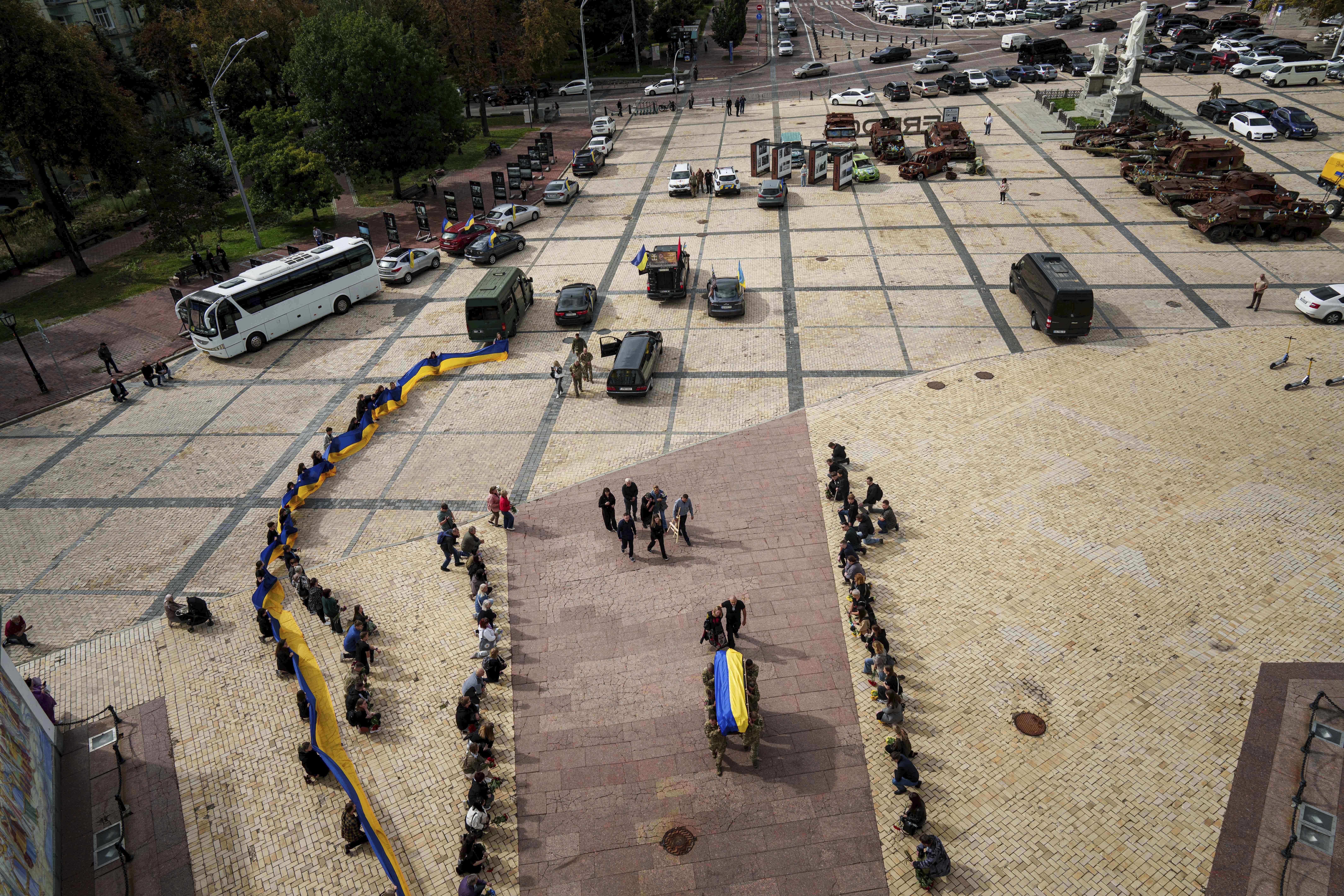 People kneel down, as honor guards carry the coffin of Artem Antonenko, a Ukrainian serviceman, during his funeral ceremony in the center of Kyiv, Ukraine, Friday, Sept. 19, 2025. (Evgeniy Maloletka - AP)