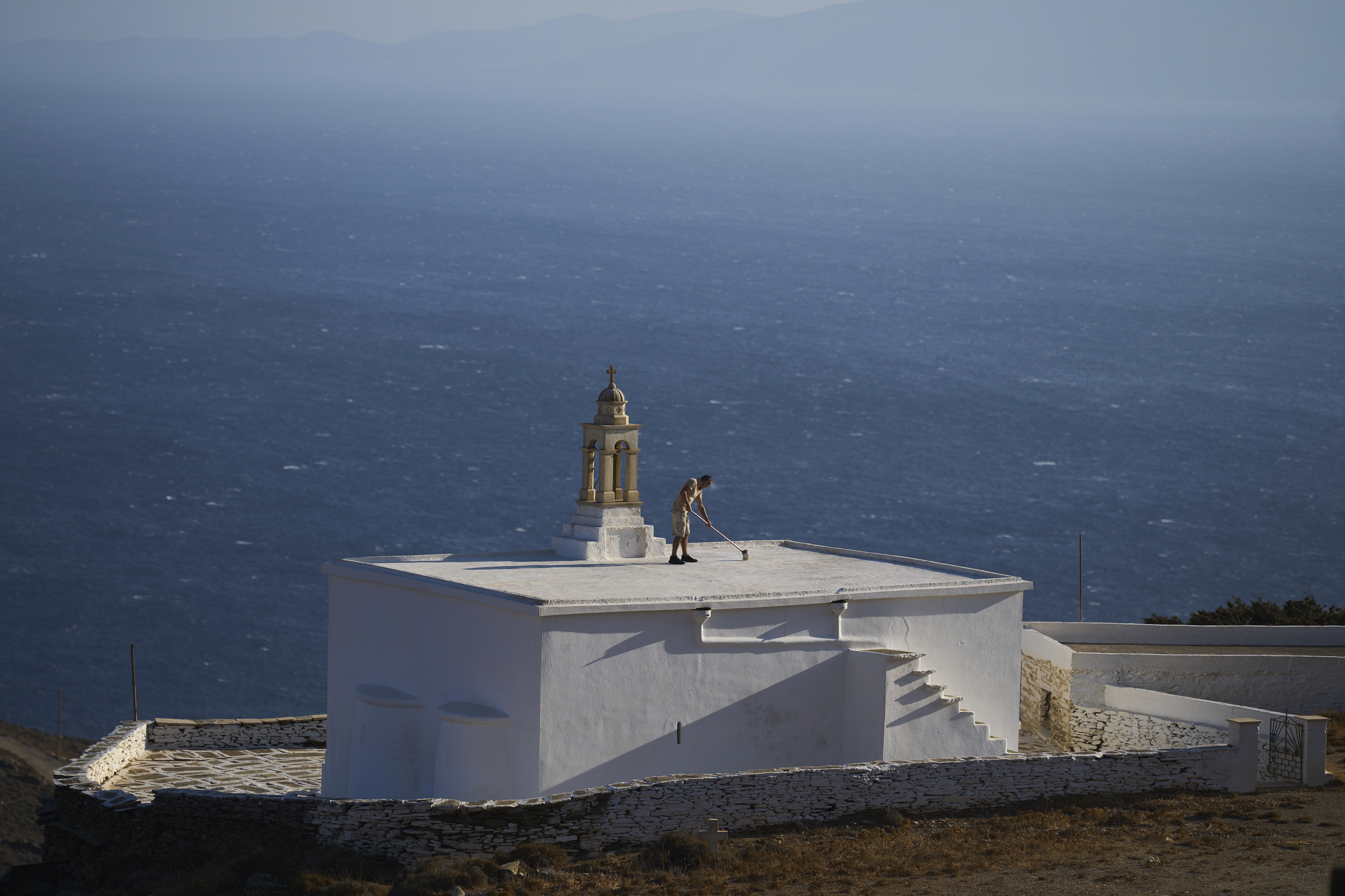Naim Domi, 50, an Albanian worker who has lived in Greece for 17 years, paints the rooftop of the Panagia Faneromeni family-owned chapel overlooking the Aegean Sea near the village of Pyrgos, on the island of Tinos, Greece, Sunday, Sept. 7, 2025. (Petros Giannakouris - AP)
