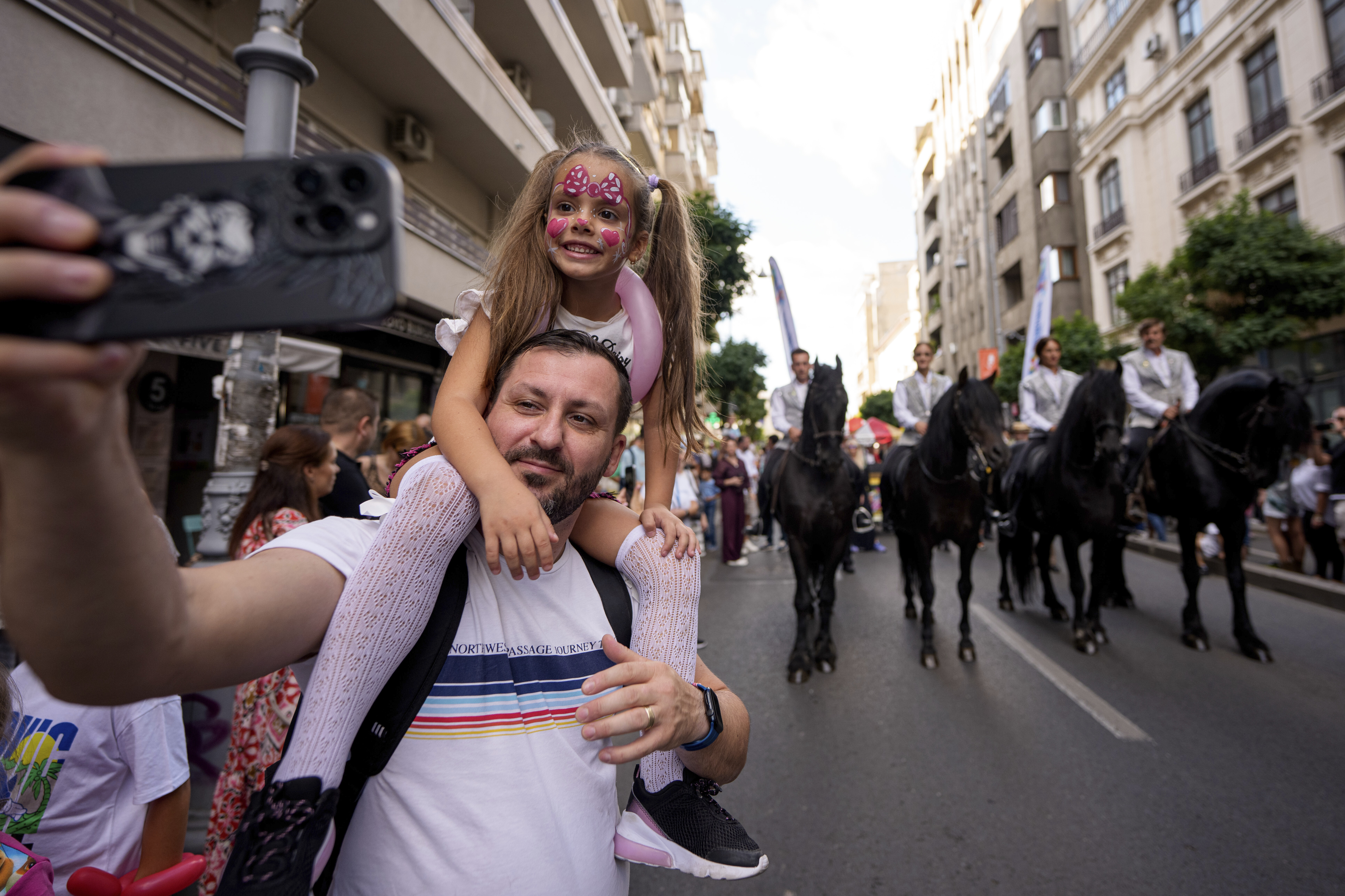 A man takes a selfie photograph with a child during a parade marking the day when the Romanian capital was first mentioned in historical records, 566 years ago, in Bucharest, Romania, Saturday, Sept. 20, 2025. (Andreea Alexandru - AP)