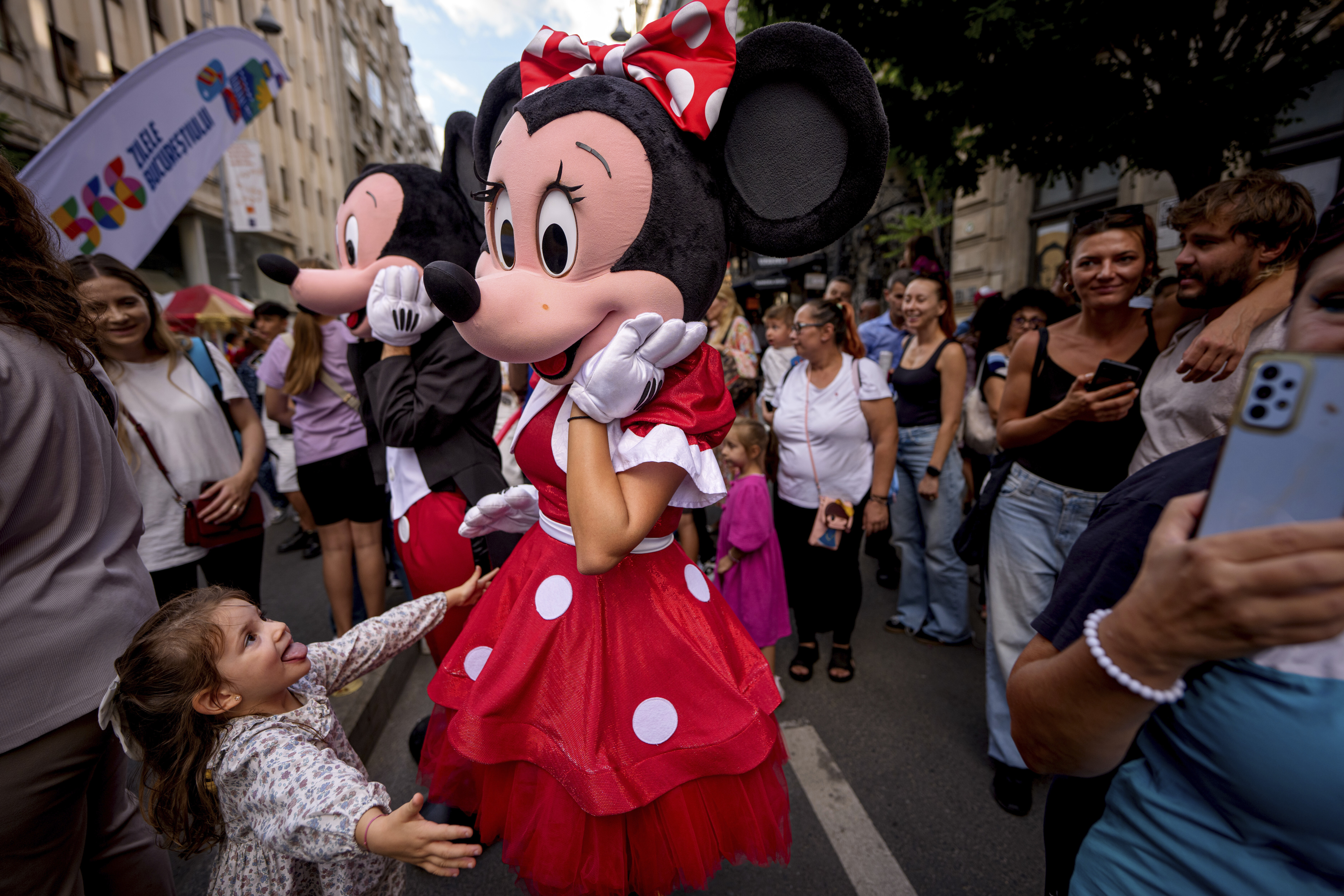 A child tries to hug an entertainer wearing a Minnie Mouse costume during a parade marking the day when the Romanian capital was first mentioned in historical records, 566 years ago, in Bucharest, Romania, Saturday, Sept. 20, 2025. (Andreea Alexandru - AP)
