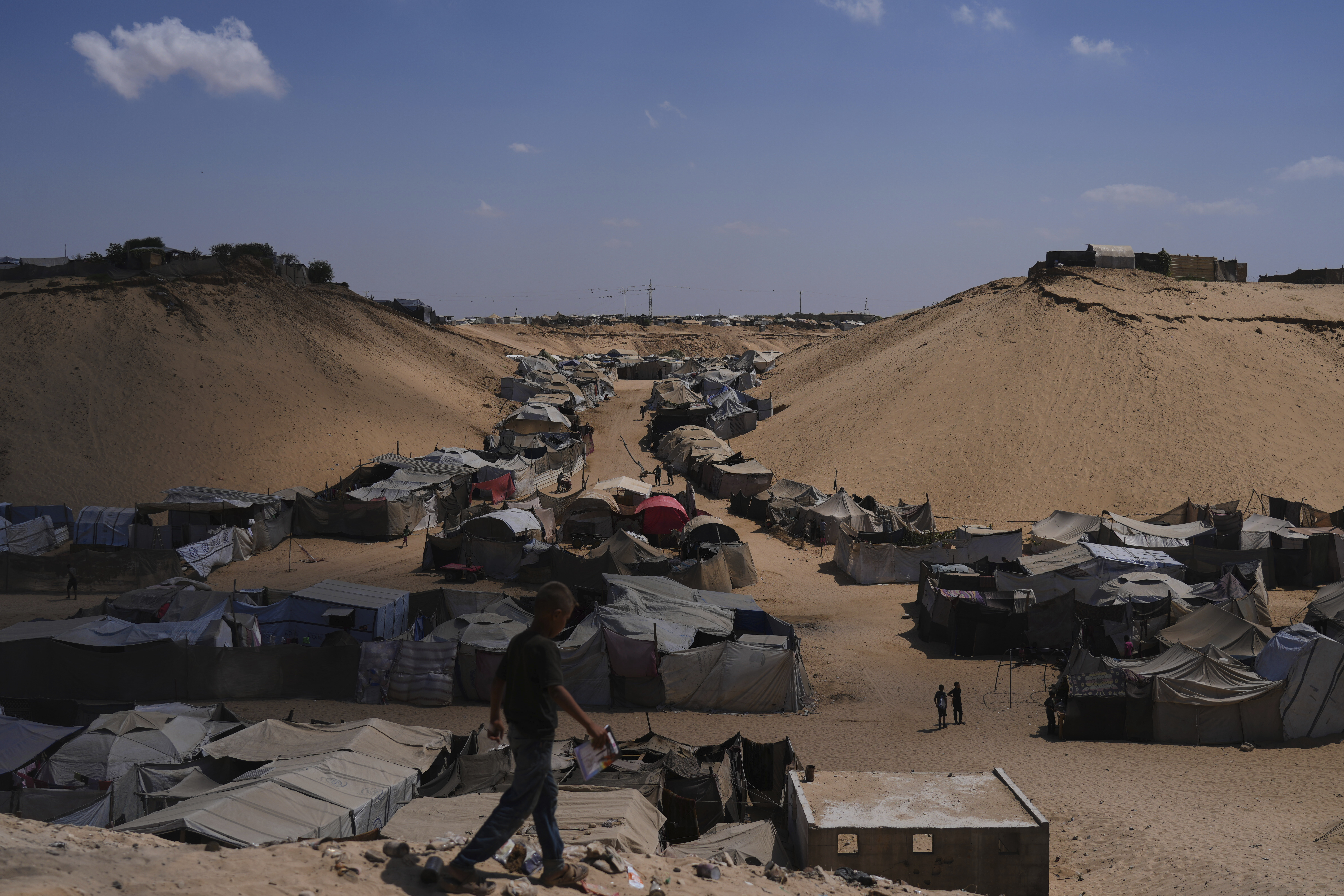 Displaced Palestinians walks through a tent camp in Muwasi, an area that Israel has designated as a safe zone, in Khan Younis southern Gaza Strip, Sunday, Sept. 21, 2025. (Jehad Alshrafi - AP)
